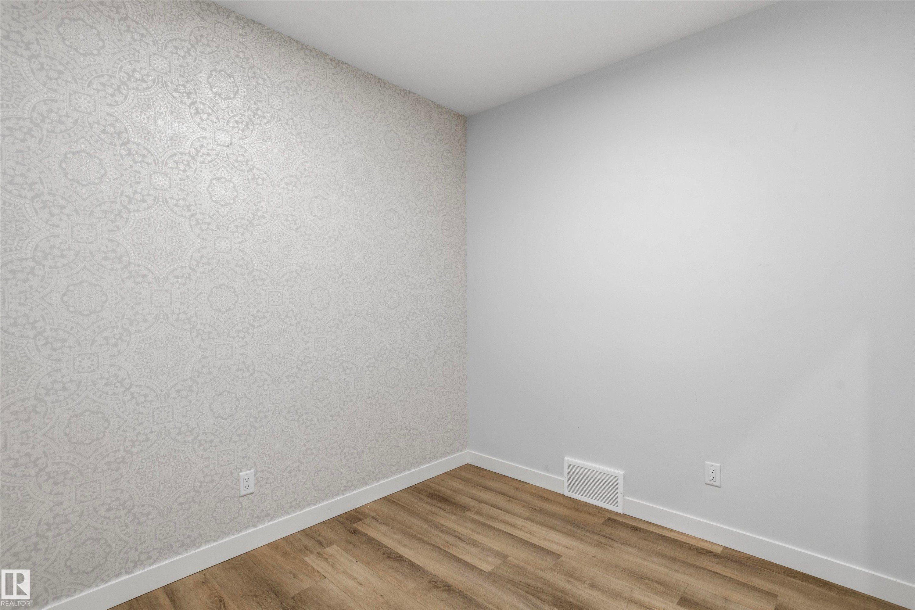 Room featuring wood-finish flooring and an accent wall with patterned wallpaper - 2045 209A St Nw, Edmonton, AB