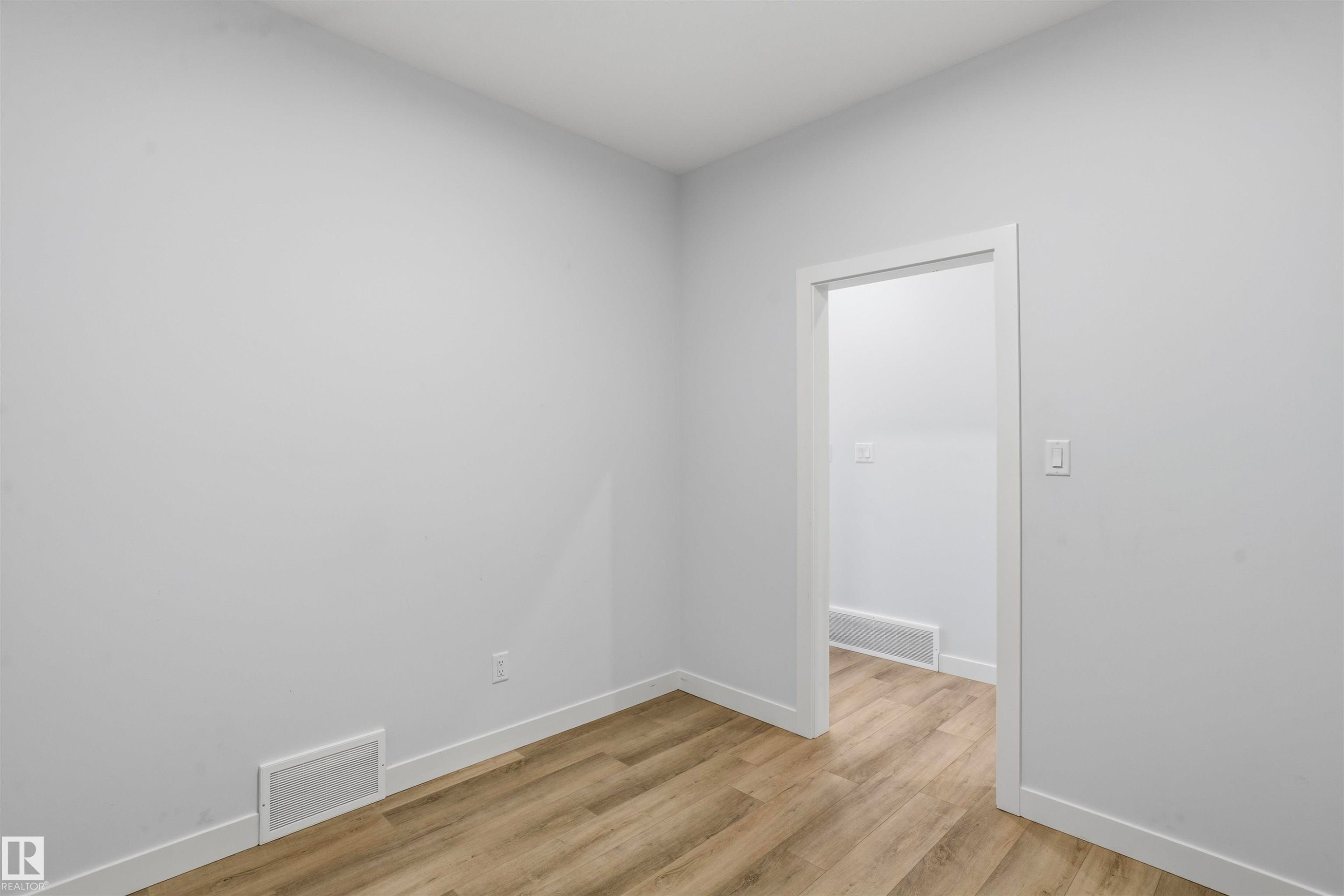Neutral-toned interior space featuring wood-finish flooring, white walls, and a doorway with a simple trim frame - 2045 209A St Nw, Edmonton, AB