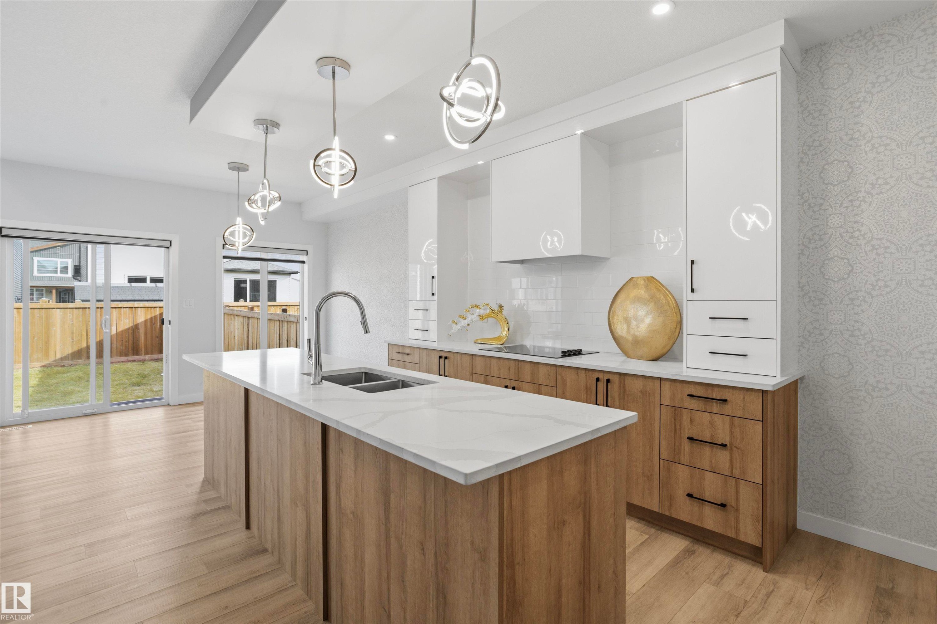 Kitchen featuring white and wood-finish cabinetry, a central island with a solid surface countertop, an undermount dual-basin sink, and modern pendant lighting - 2045 209A St Nw, Edmonton, AB
