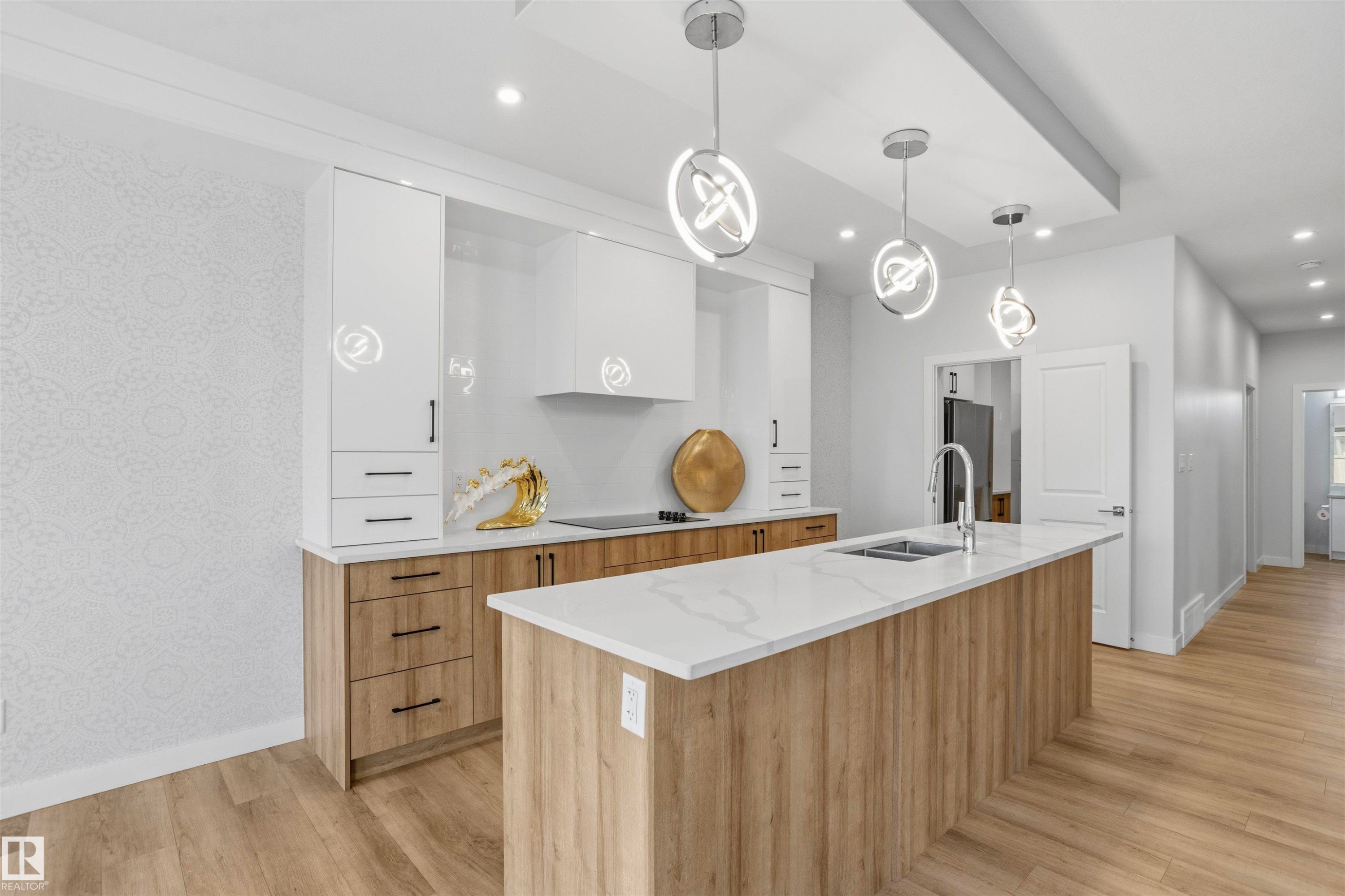 Kitchen featuring two-tone cabinetry, central island with light-toned countertop, integrated range hood, wood-finish flooring, and pendant lighting - 2045 209A St Nw, Edmonton, AB