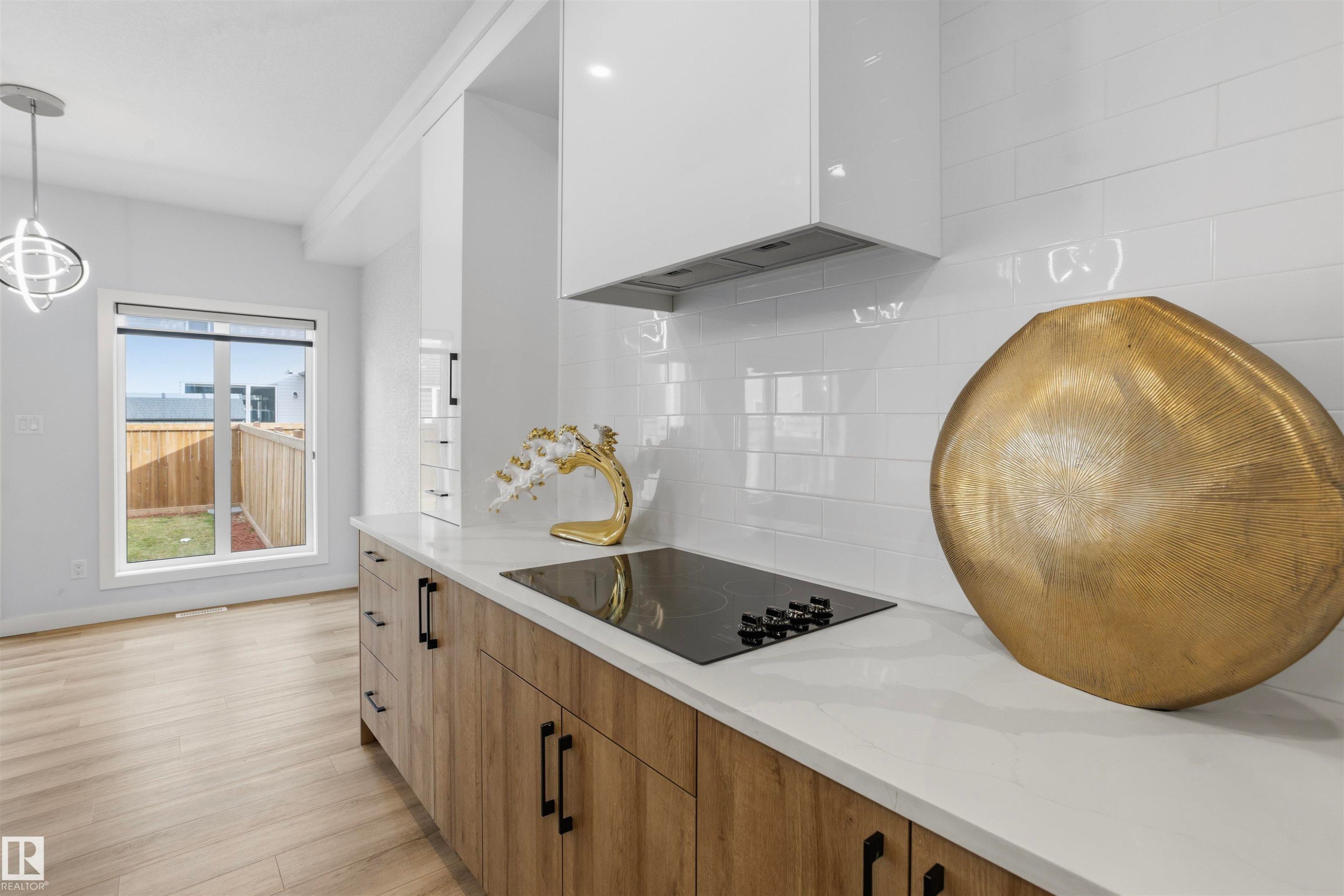 Kitchen featuring flat-panel wood-finish cabinetry, quartz countertops, white subway tile backsplash, glass cooktop, and wood-finish flooring - 2045 209A St Nw, Edmonton, AB
