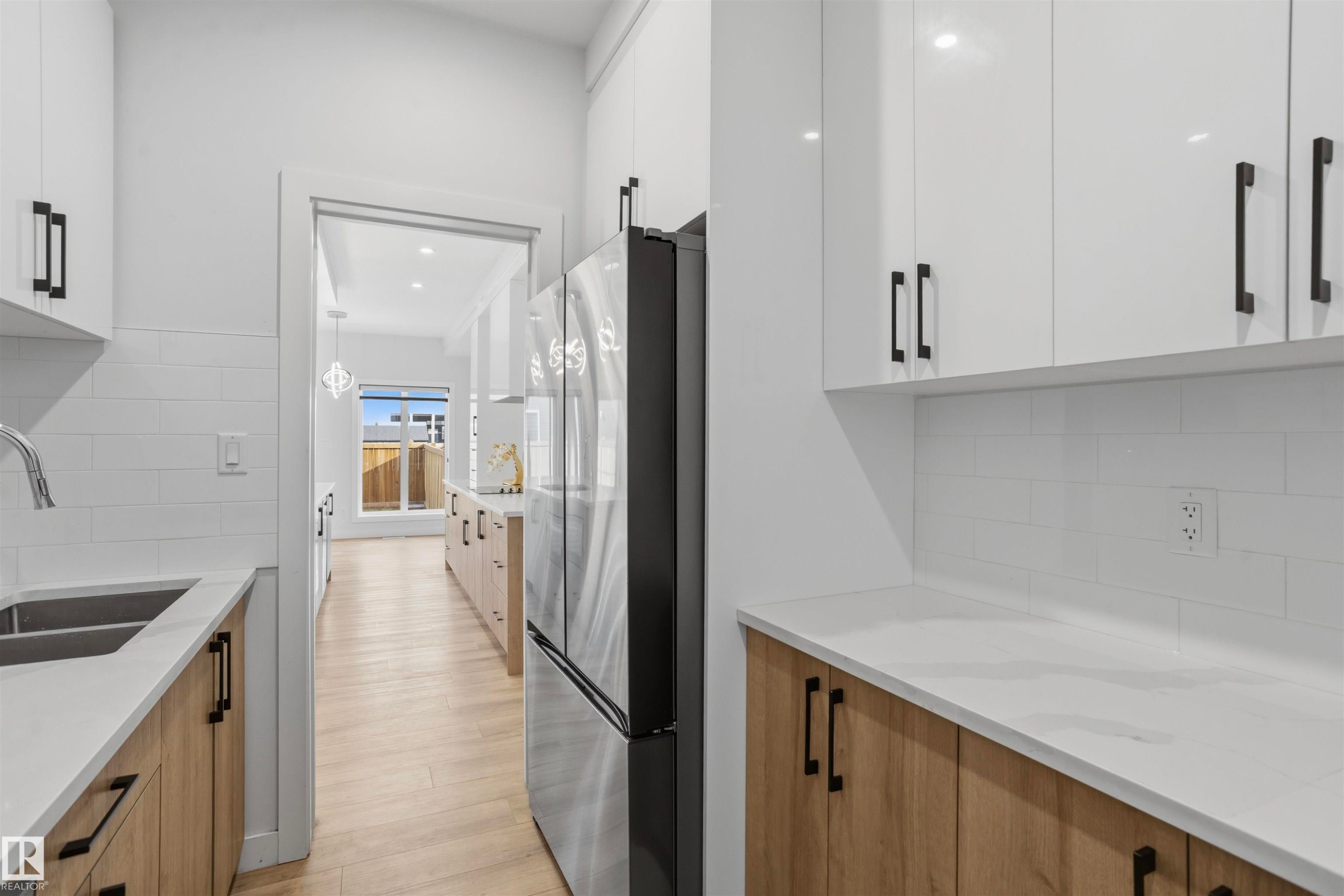 Kitchen featuring high-gloss white upper cabinetry, wood-finish lower cabinetry, white quartz countertops, subway tile backsplash, and matte black hardware - 2045 209A St Nw, Edmonton, AB