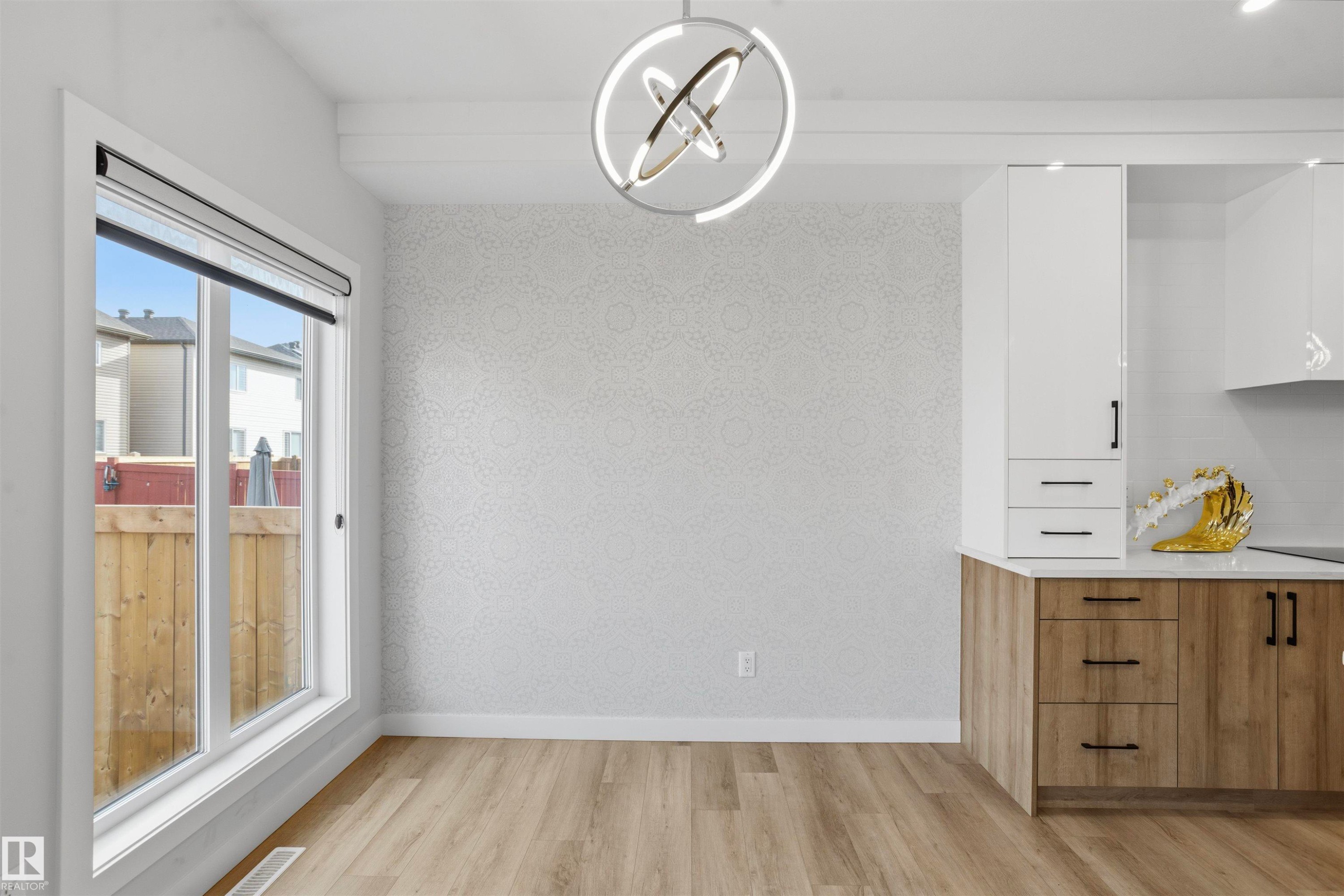 Modern ring-style chandelier, textured wall covering, wood-finish flooring, two-tone cabinetry with matte black hardware, and expansive picture window - 2045 209A St Nw, Edmonton, AB