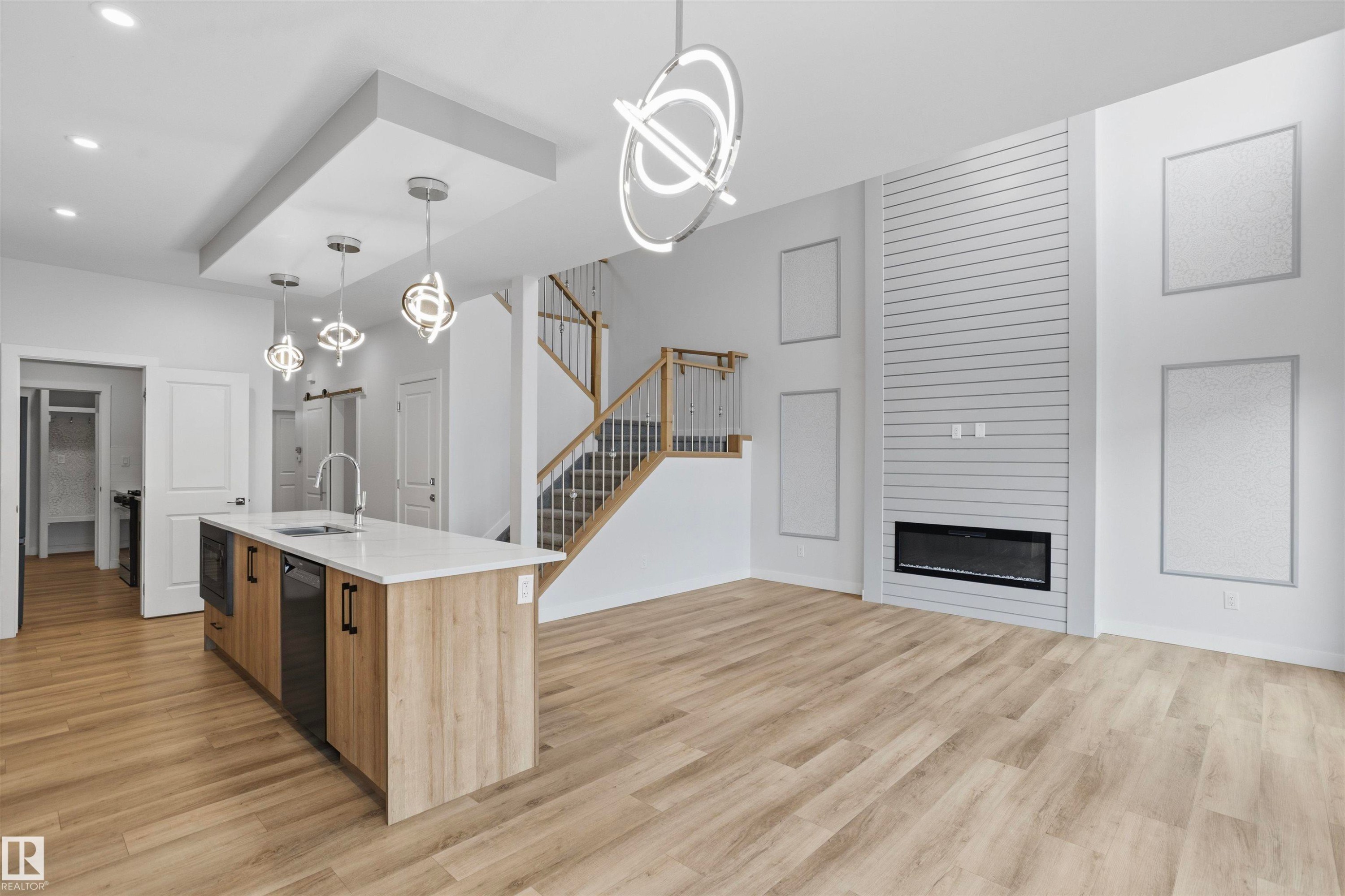 Kitchen featuring a center island with quartz countertops, wood-finish cabinetry, linear fireplace with shiplap surround, wood-finish flooring, and modern geometric pendant lighting - 2045 209A St Nw, Edmonton, AB