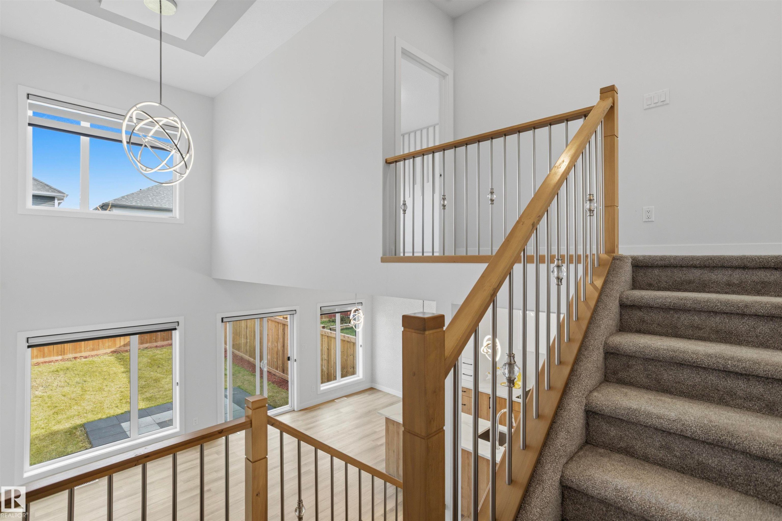 Double-height ceiling with contemporary metal sphere pendant lighting, staircase featuring wood handrails with metal balusters, and expansive windows - 2045 209A St Nw, Edmonton, AB