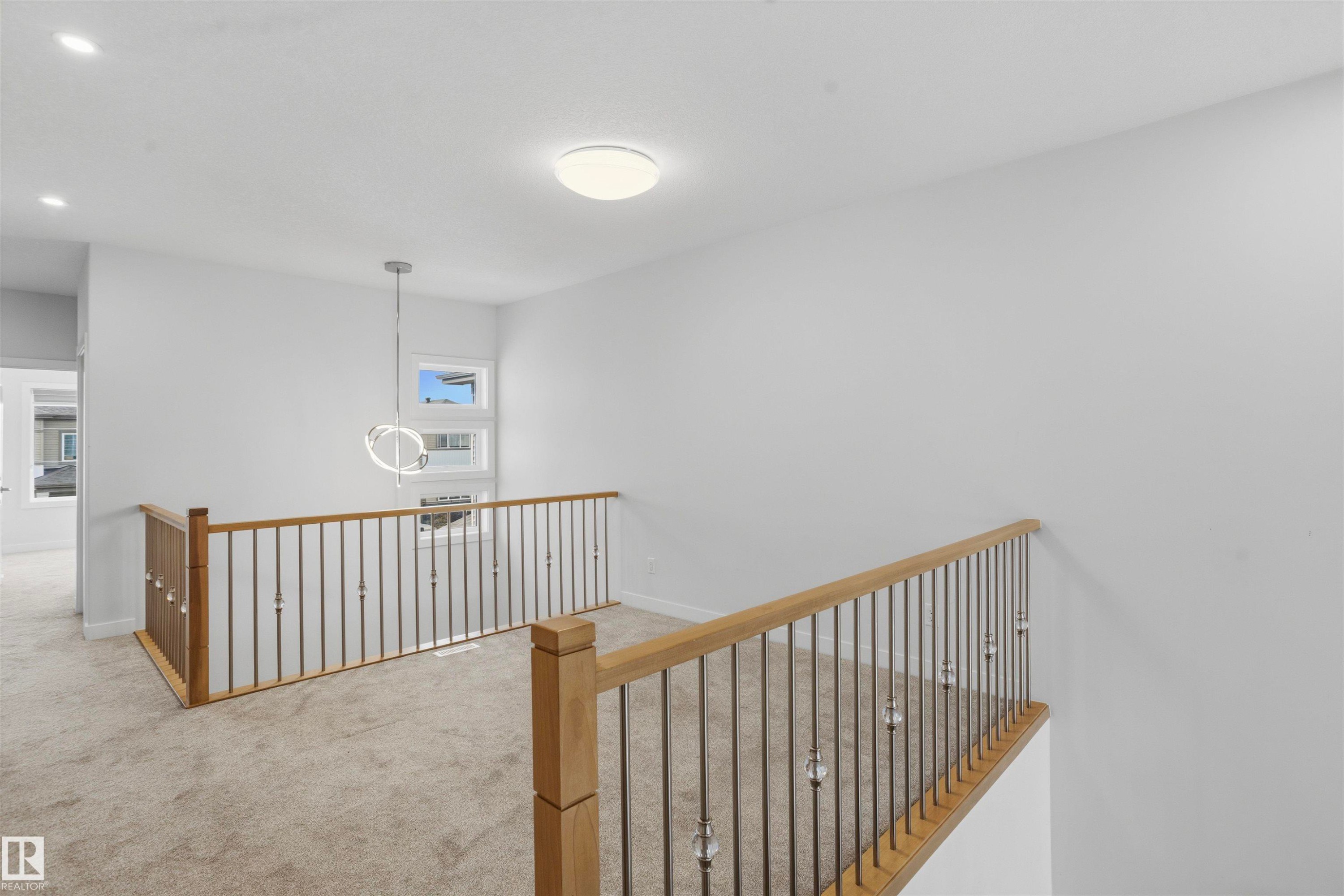 Open interior space featuring light-colored carpet flooring, recessed lighting, and a modern circular pendant fixture - 2045 209A St Nw, Edmonton, AB