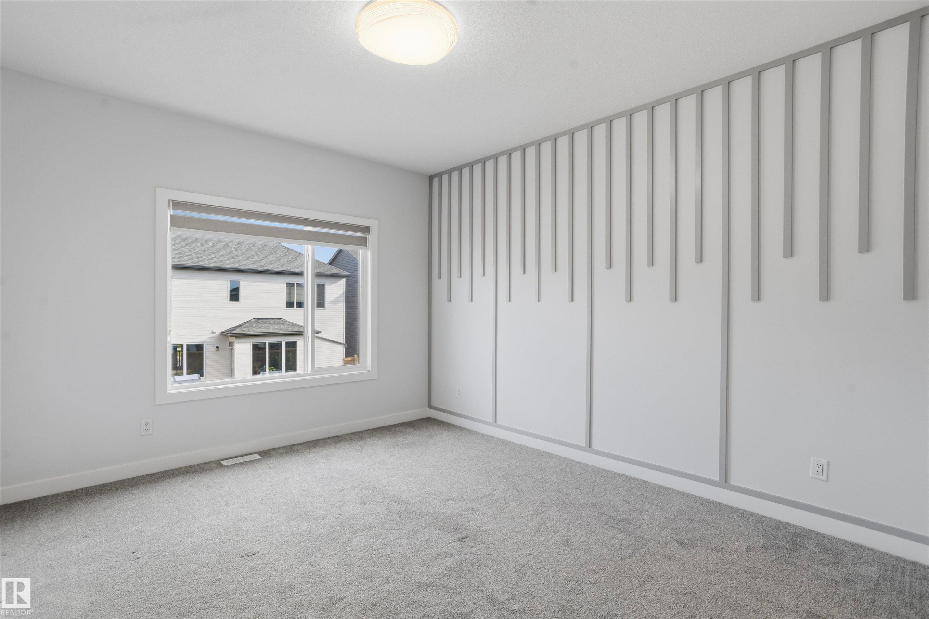 Interior room featuring carpeted flooring, a large window, a ceiling-mounted light fixture, and a decorative vertical slat accent wall - 2045 209A St Nw, Edmonton, AB