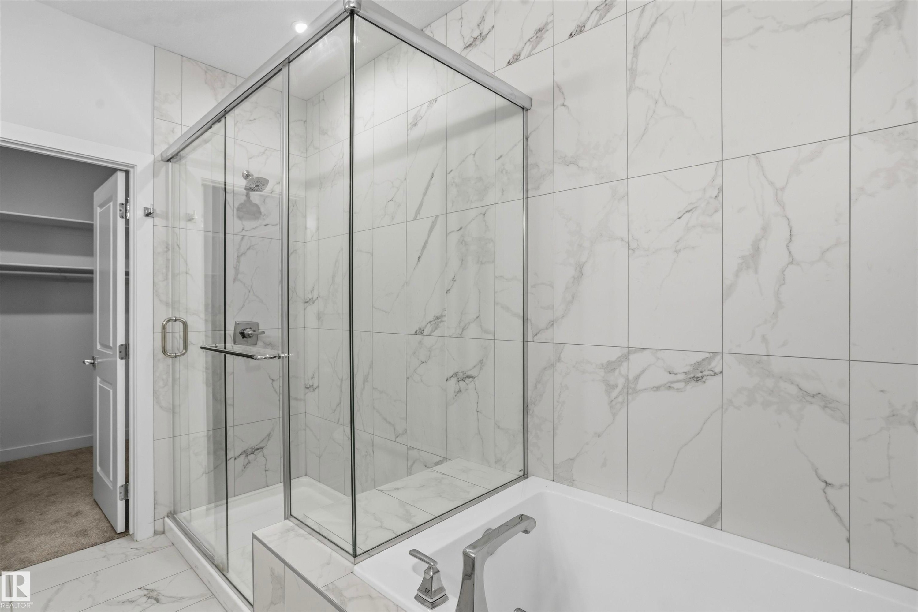 Walk-in shower with a glass enclosure, floor-to-ceiling large-format tile surround, inset soaking tub with metal hardware, and patterned tile flooring - 2045 209A St Nw, Edmonton, AB
