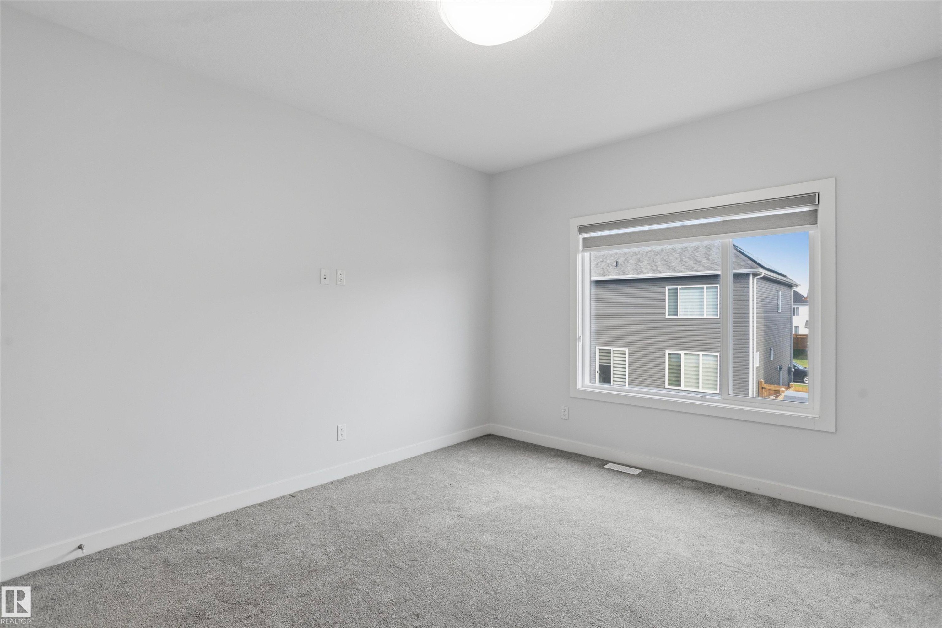 Neutral-toned interior space featuring neutral wall-to-wall carpeting, crisp white walls, and a large horizontal sliding window with an integrated roller shade - 2045 209A St Nw, Edmonton, AB