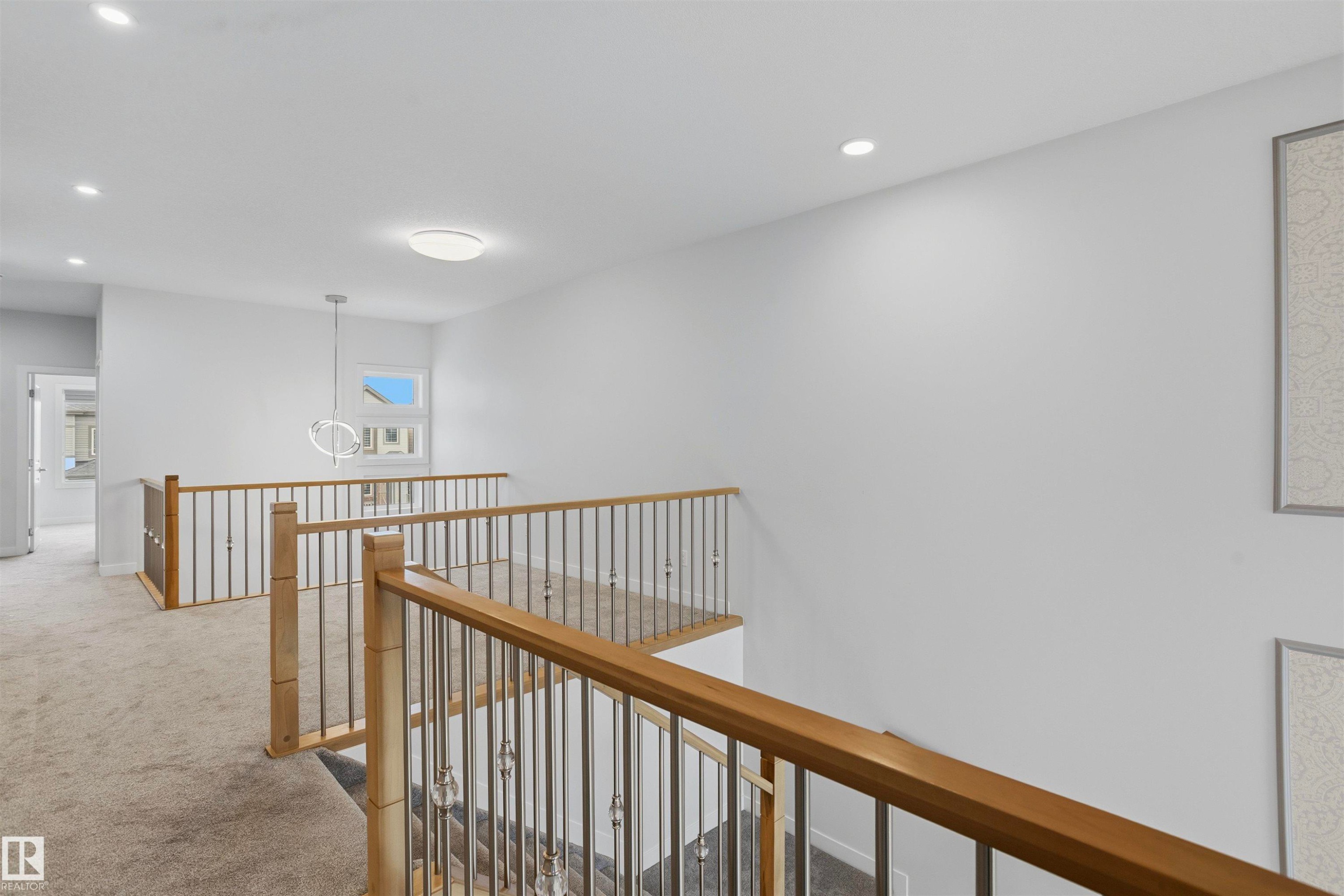 Landing featuring carpeted flooring, wood-topped railing with metal balusters, recessed lighting, and contemporary pendant fixture - 2045 209A St Nw, Edmonton, AB
