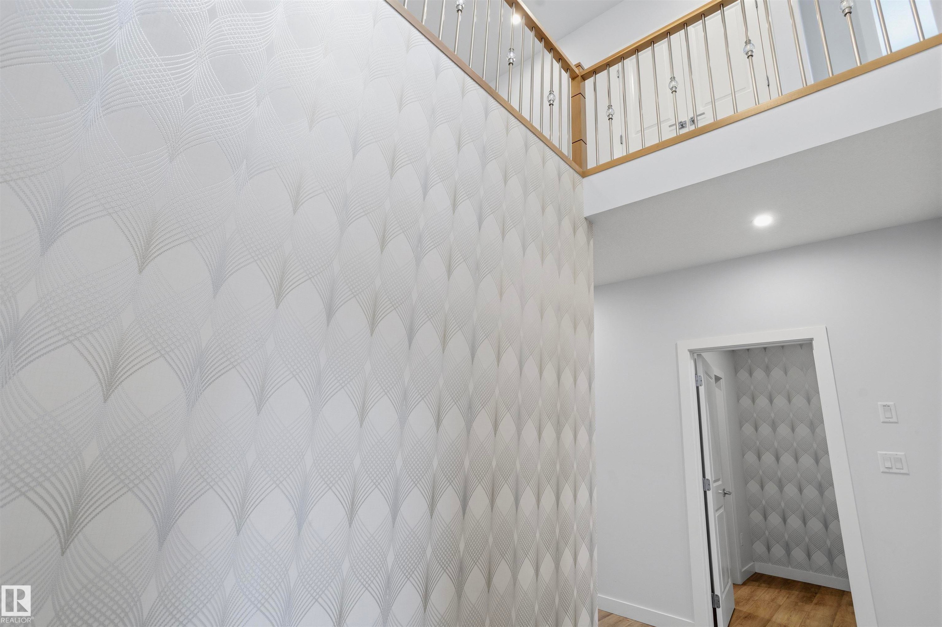 Double-height ceiling, geometric-patterned wallpaper, wooden railing with vertical balusters, recessed lighting, and wood-finish flooring - 2045 209A St Nw, Edmonton, AB