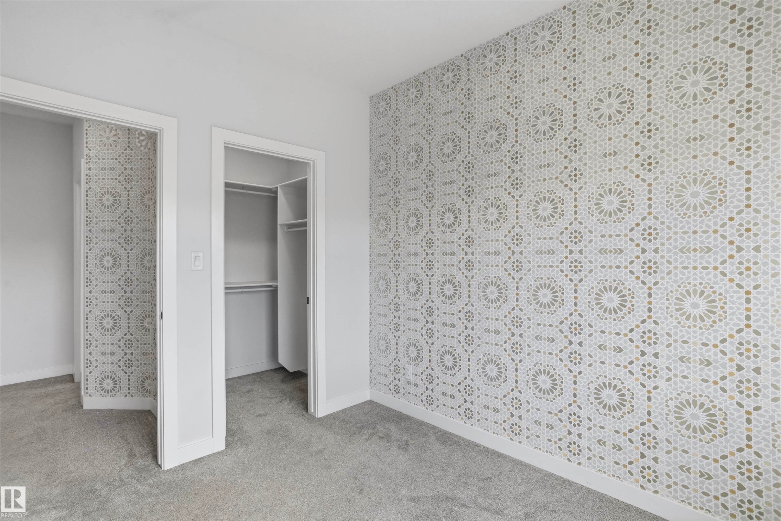 Accent wall featuring geometric patterned wallpaper, neutral carpeting, and a built-in closet system - 2045 209A St Nw, Edmonton, AB