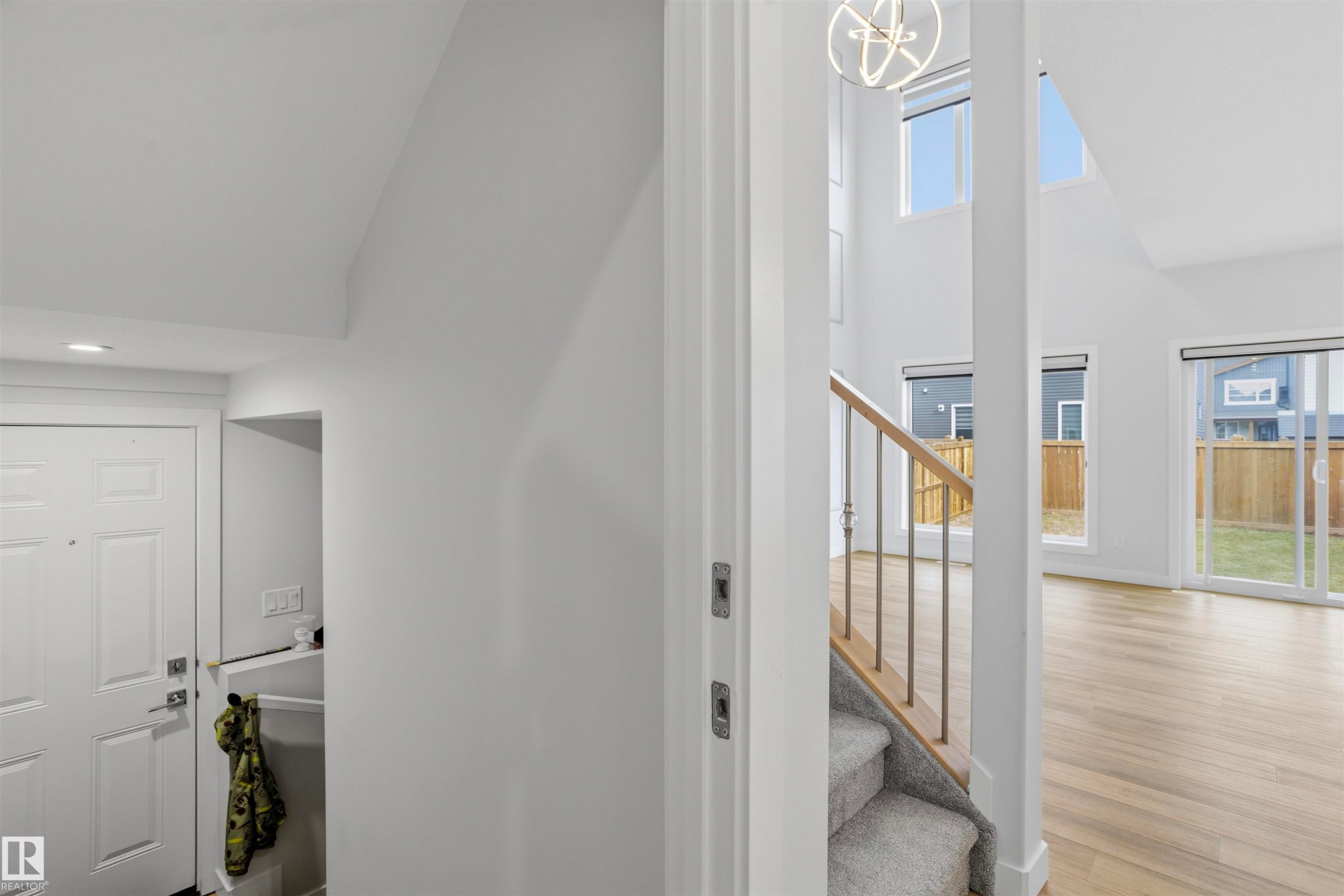 High-ceilinged interior featuring wood-finish flooring, staircase with a wooden handrail, multi-pane windows, and geometric pendant lighting - 2045 209A St Nw, Edmonton, AB