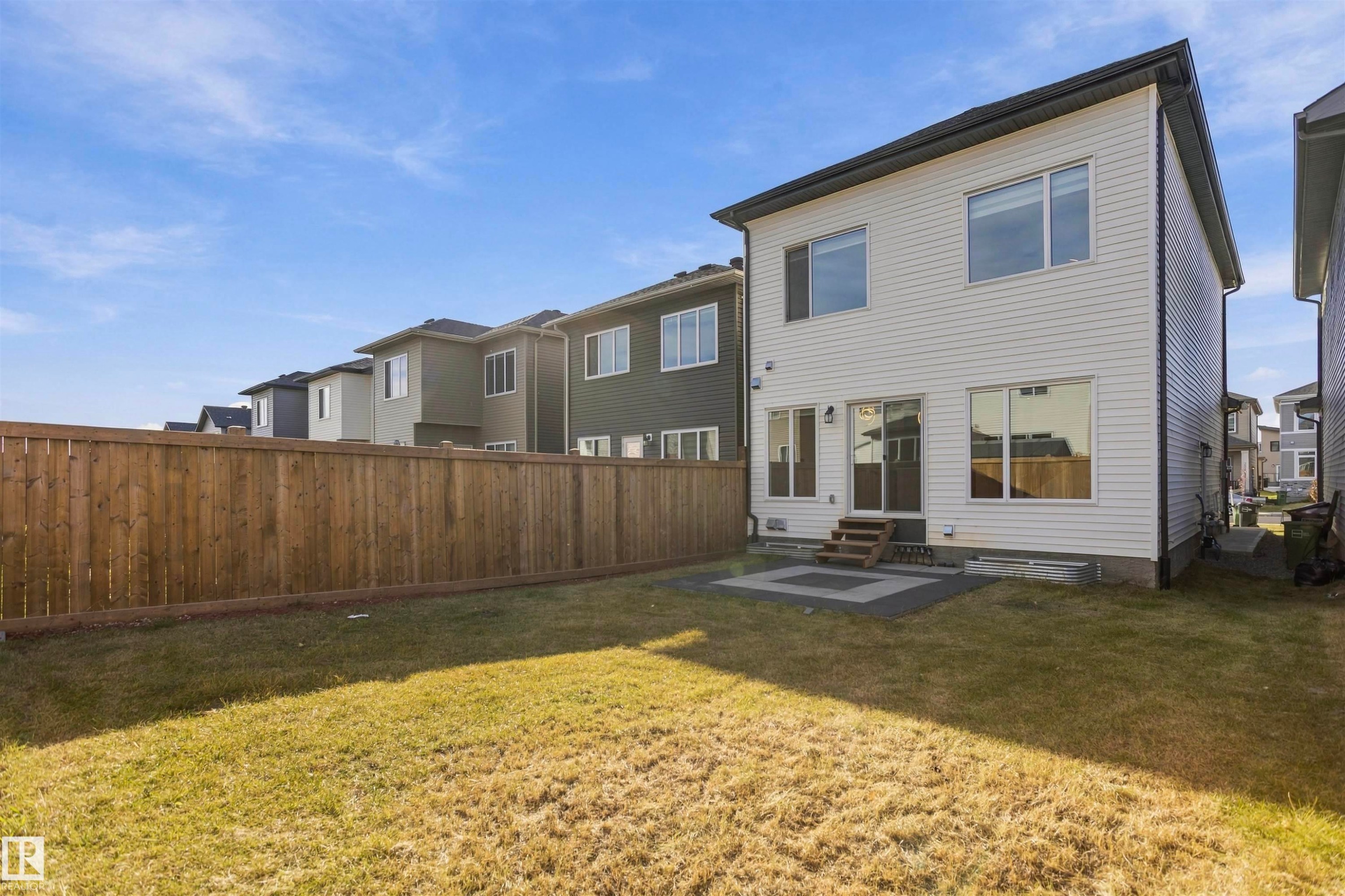 Rear exterior featuring horizontal vinyl siding, a fully fenced backyard, a paved stone patio, and wood-step entry - 2045 209A St Nw, Edmonton, AB
