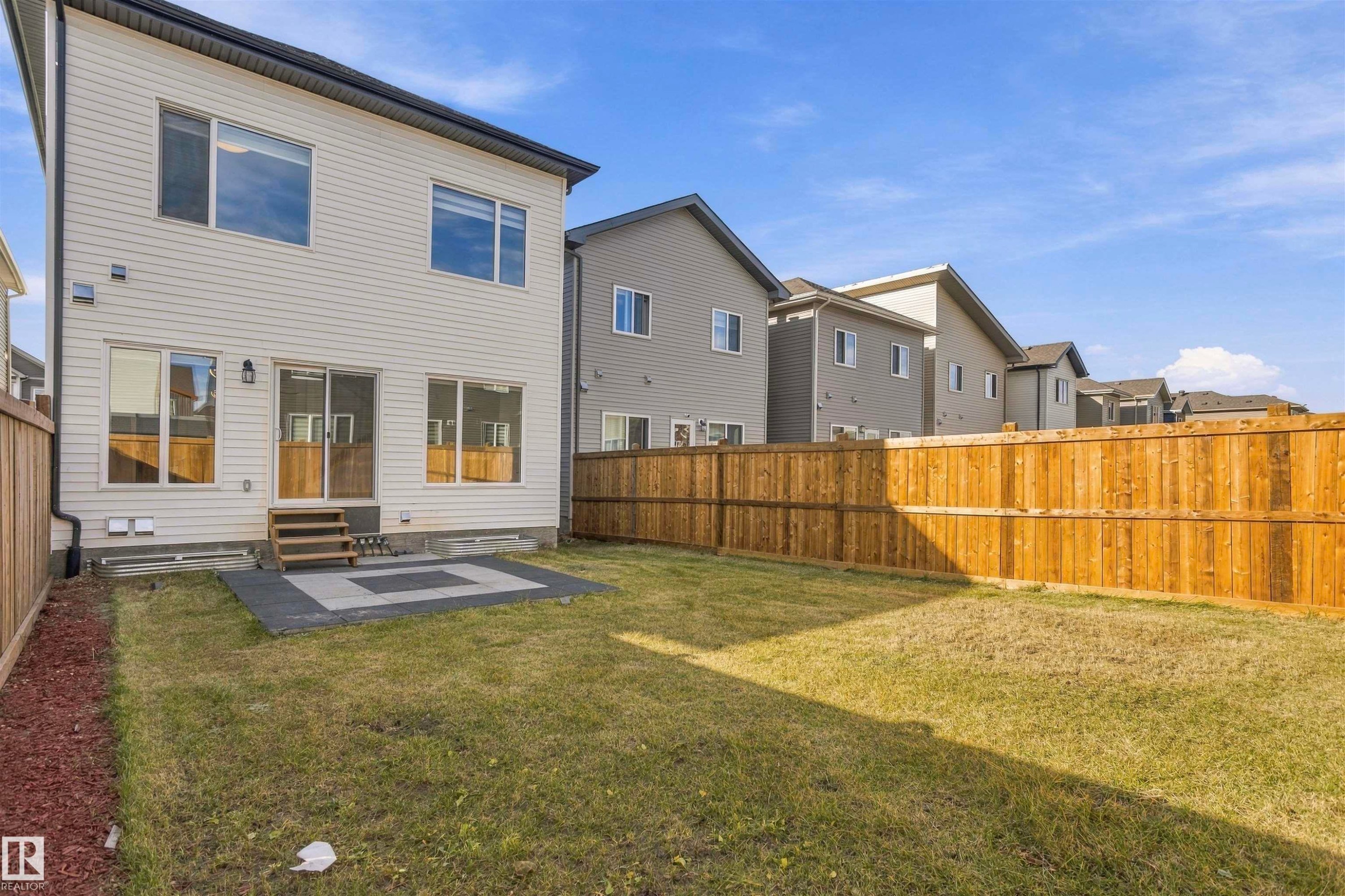 Rear exterior featuring horizontal lap siding, a paved patio, and a fully enclosed wood fence - 2045 209A St Nw, Edmonton, AB