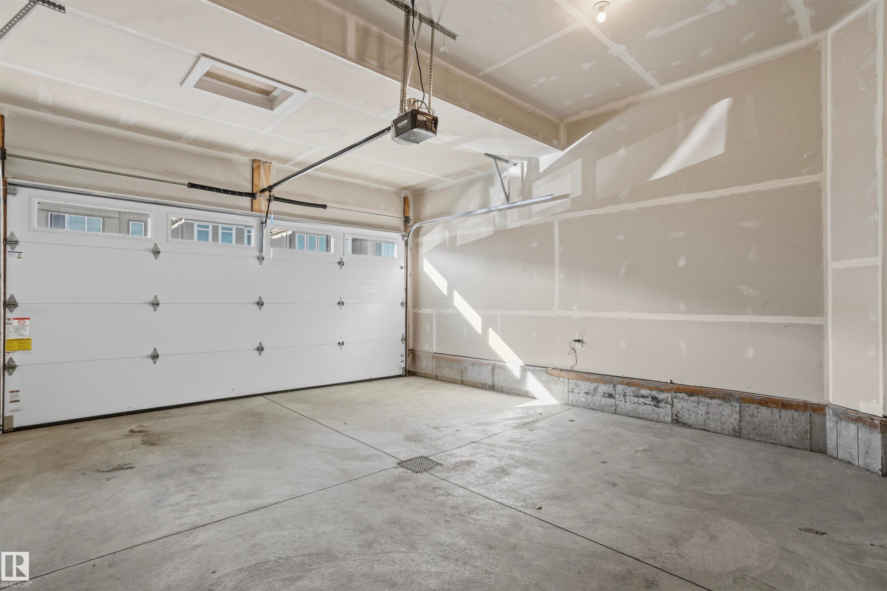 Two-car garage featuring a concrete floor, high ceilings, automated door with integrated windows, and drywall finish - 2045 209A St Nw, Edmonton, AB