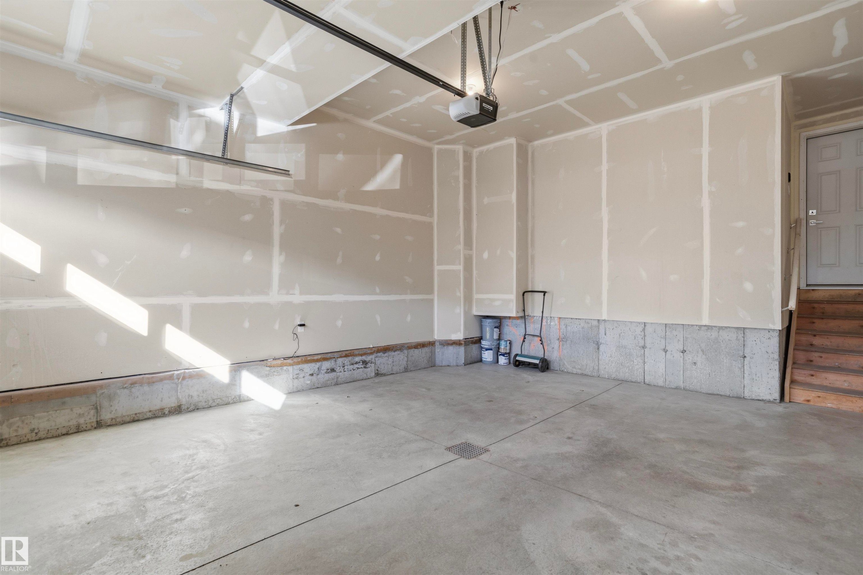 Garage featuring a concrete floor, finished drywall, automatic door opener, and wooden stairs - 2045 209A St Nw, Edmonton, AB