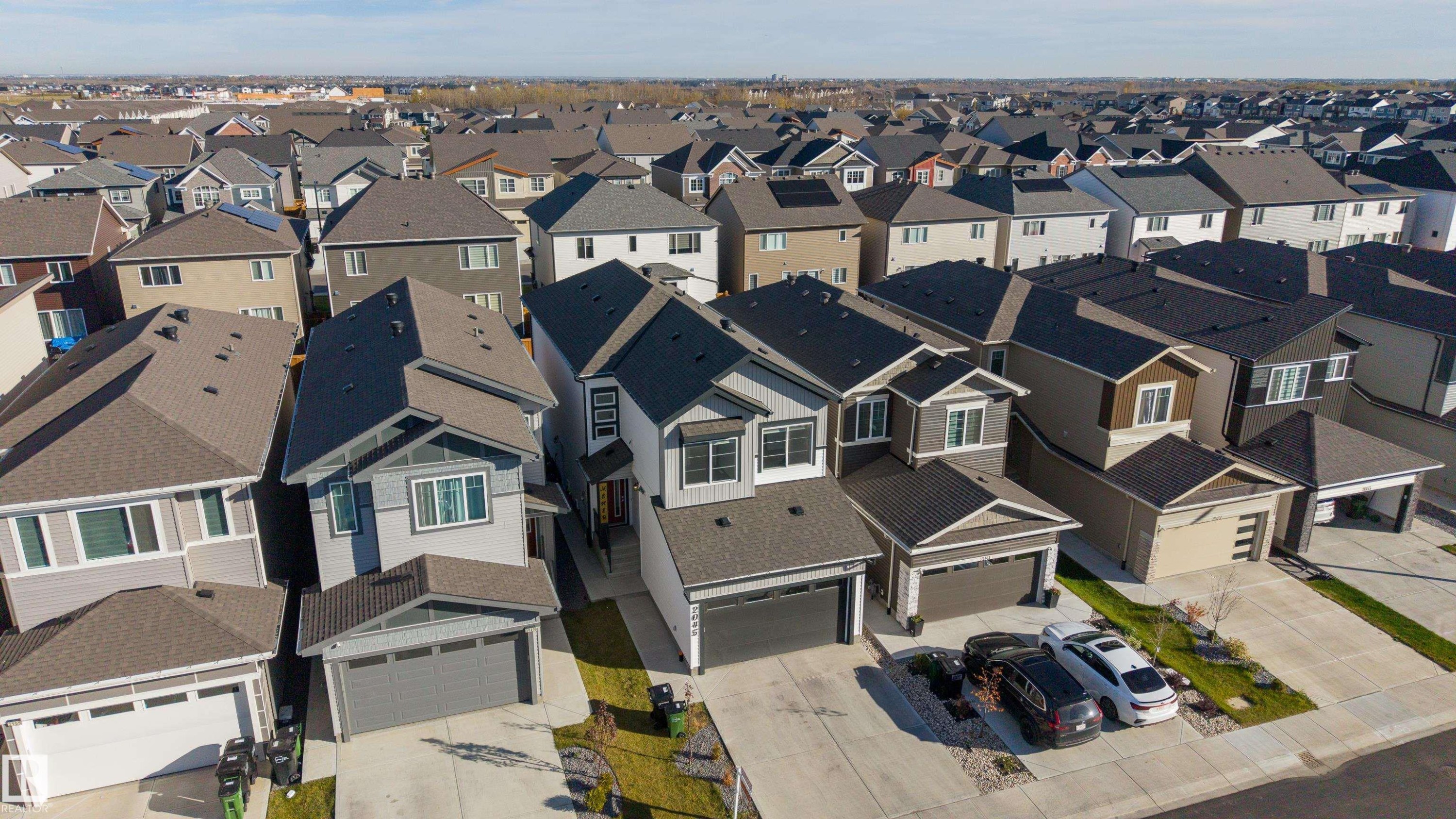 Aerial perspective of a multi-level suburban residence featuring a concrete driveway, attached garage, shingled roofing, and a neutral-toned exterior facade - 2045 209A St Nw, Edmonton, AB