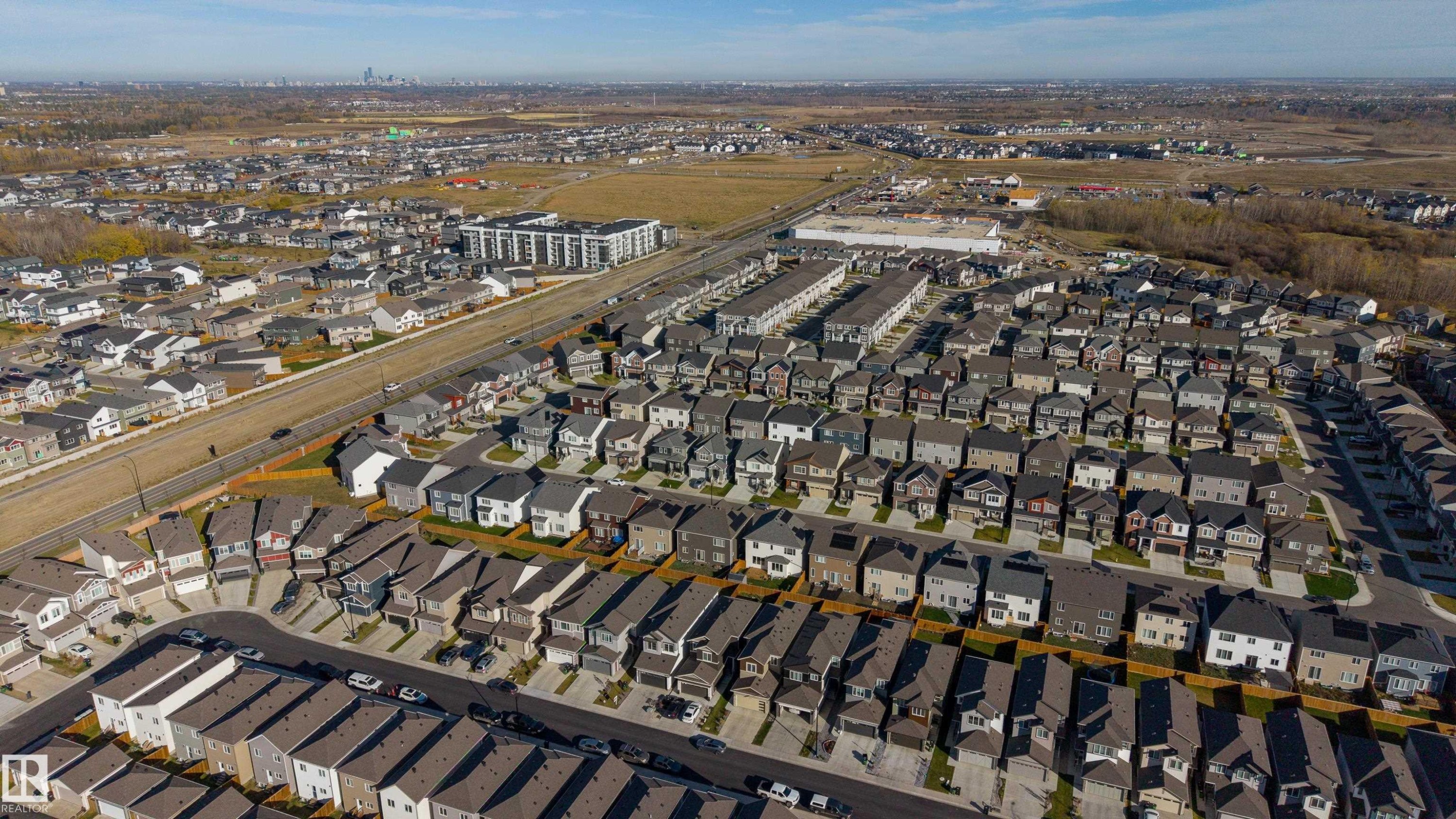 Aerial perspective of a planned suburban residential development featuring multi-level dwellings, grid-patterned streets, concrete driveways, and expansive regional horizon lines - 2045 209A St Nw, Edmonton, AB