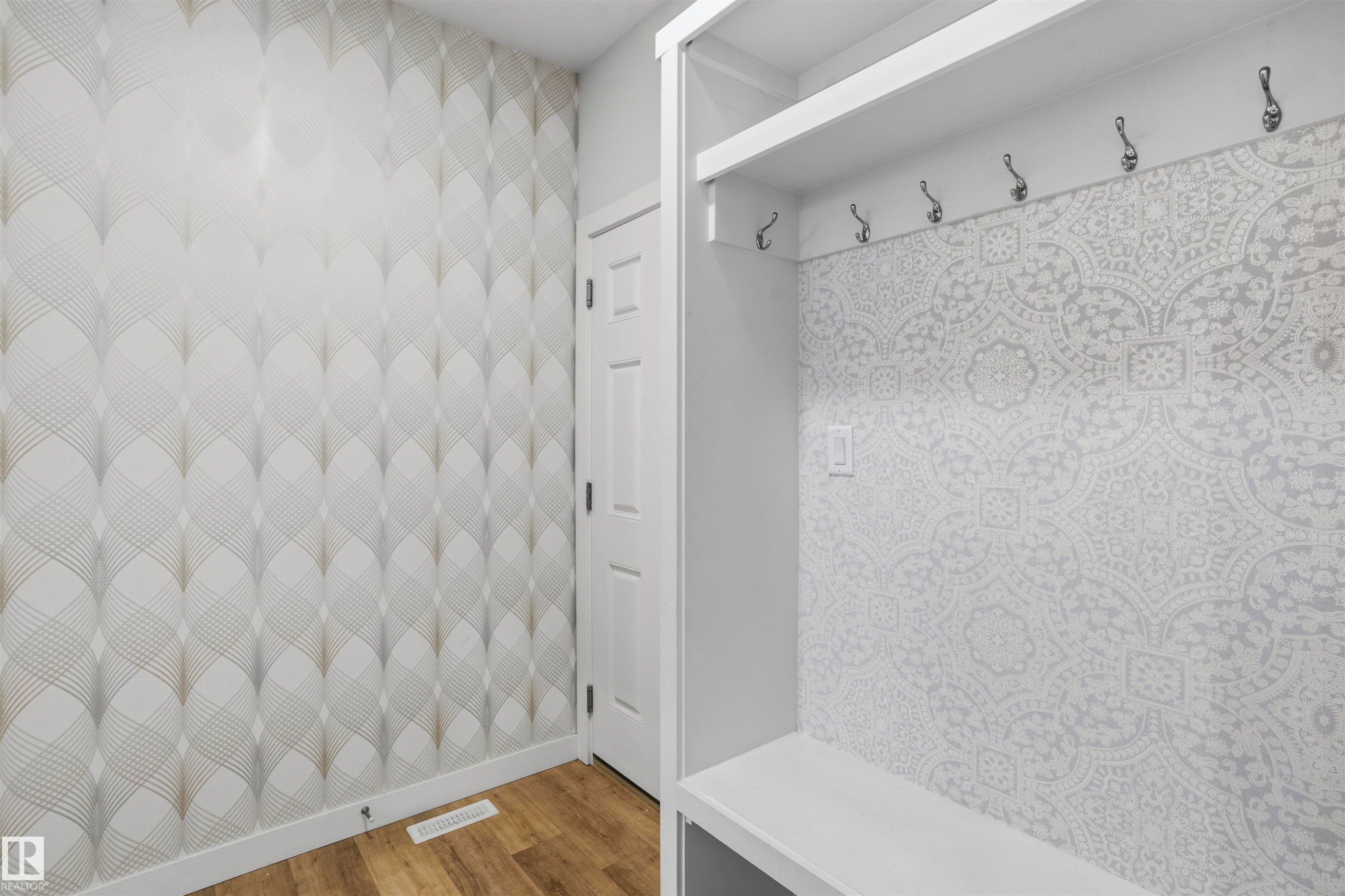 Built-in mudroom bench with overhead shelving and six mounted hooks, featuring patterned accent wallpaper and wood-finish flooring - 2045 209A St Nw, Edmonton, AB