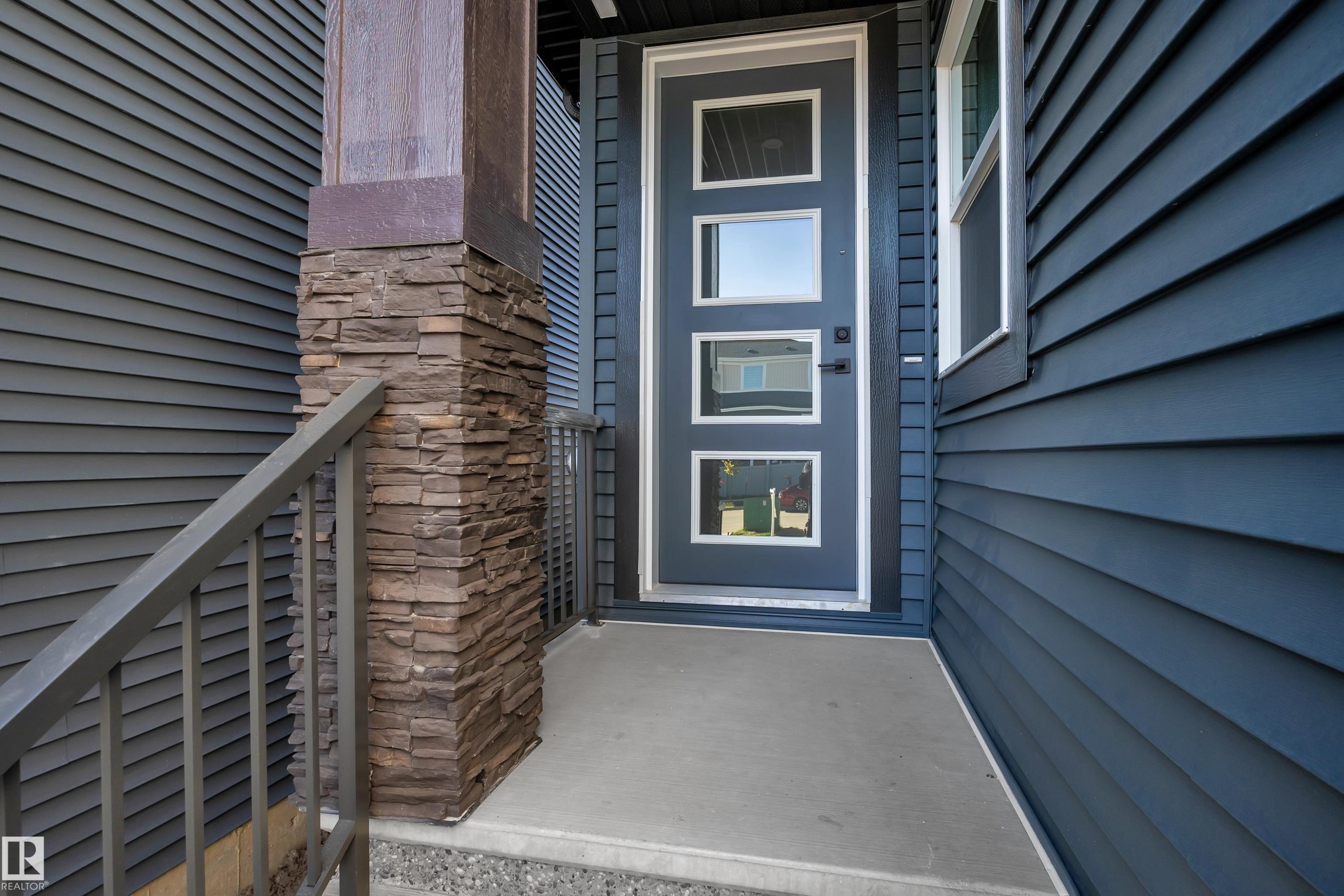 Modern front entry featuring a multi-pane door, horizontal siding, and a stone-clad pillar - 3604 44 Avenue, Beaumont, AB