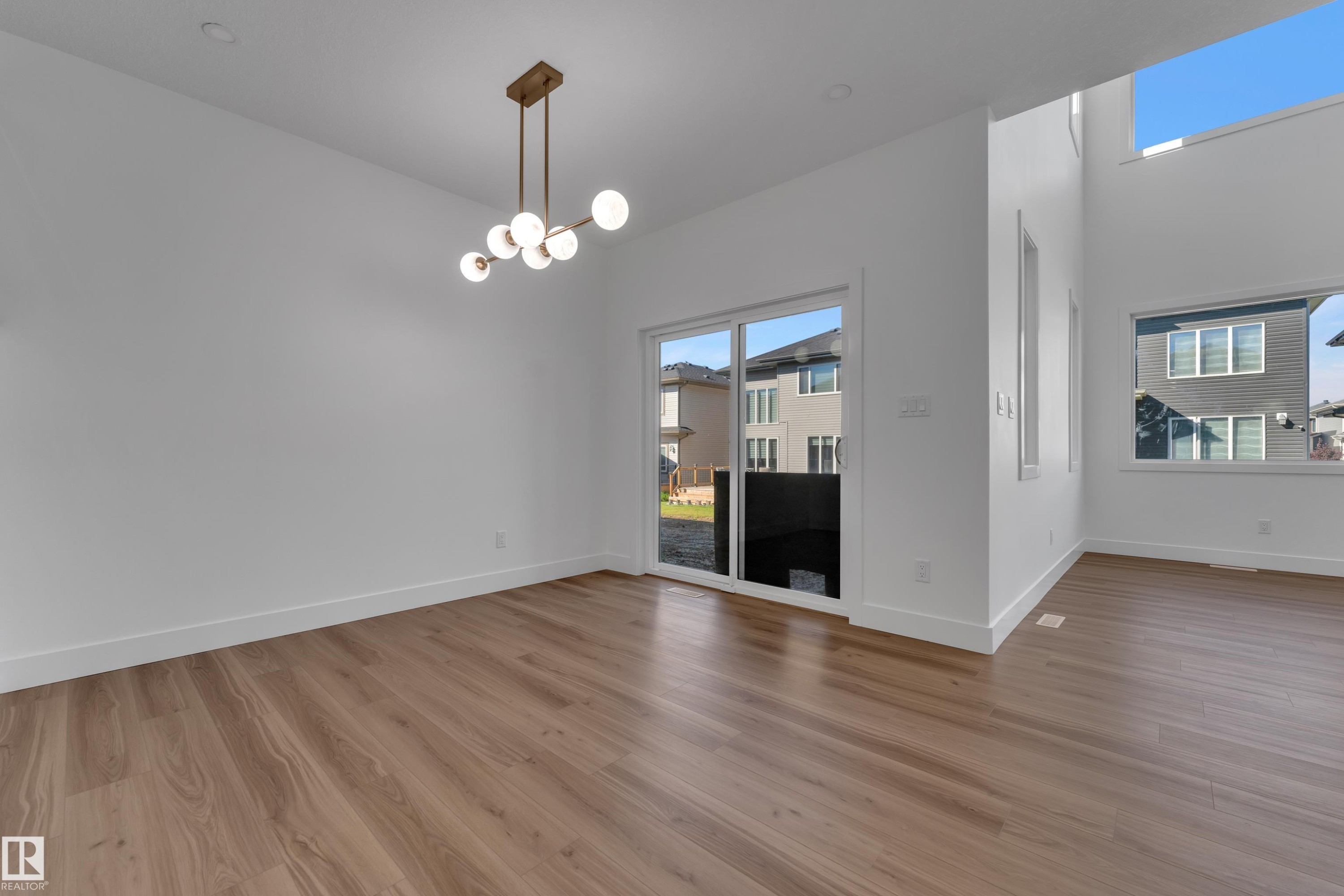 Wood-finish flooring with a modern ceiling light fixture, featuring multiple windows and a sliding glass door - 3604 44 Avenue, Beaumont, AB