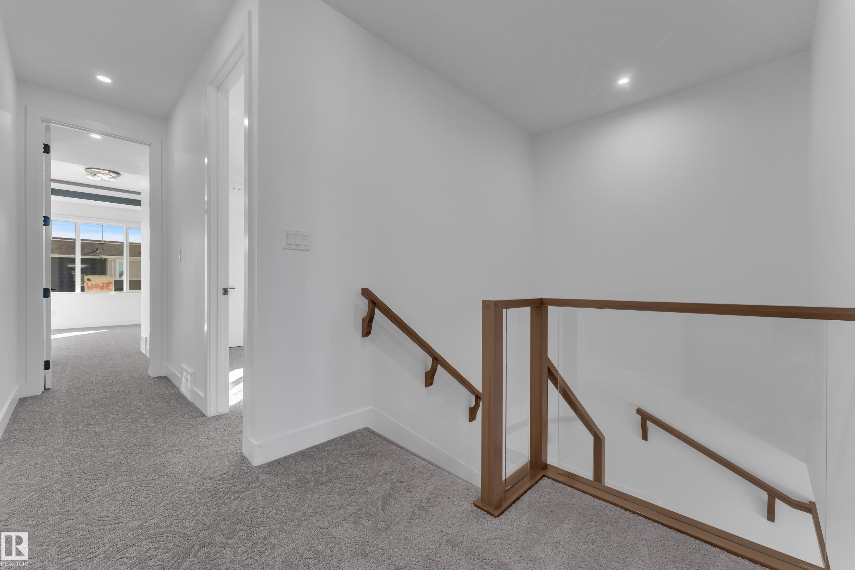Wall-to-wall patterned carpeting, recessed ceiling lighting, a clear glass stair railing with wood-finish top and bottom rails, and a wood-finish handrail - 3604 44 Avenue, Beaumont, AB