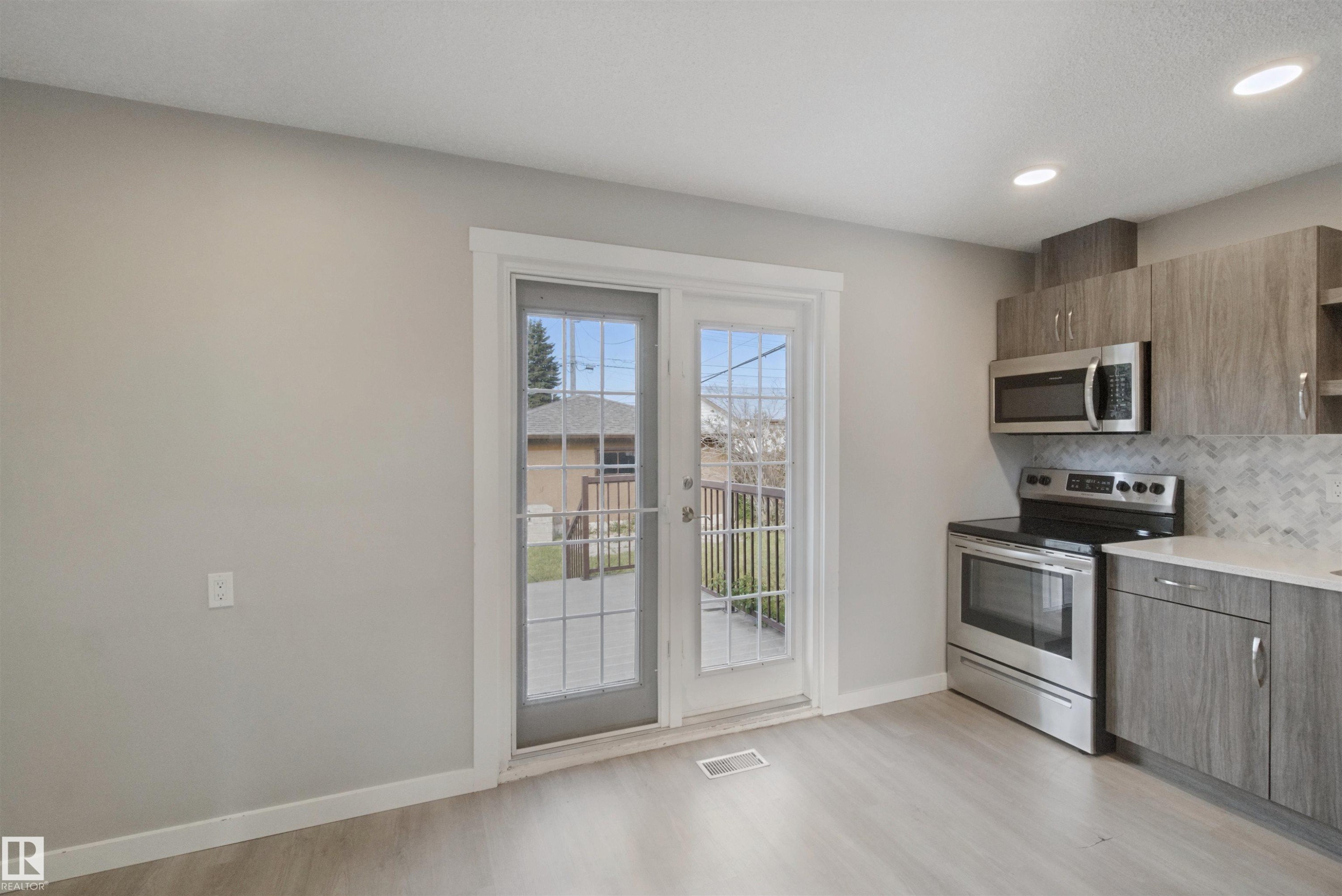 Kitchen featuring wood-finish cabinetry, stainless steel appliances, a patterned tile backsplash, recessed lighting, and patio doors - 13212 73 Street Nw, Edmonton, AB