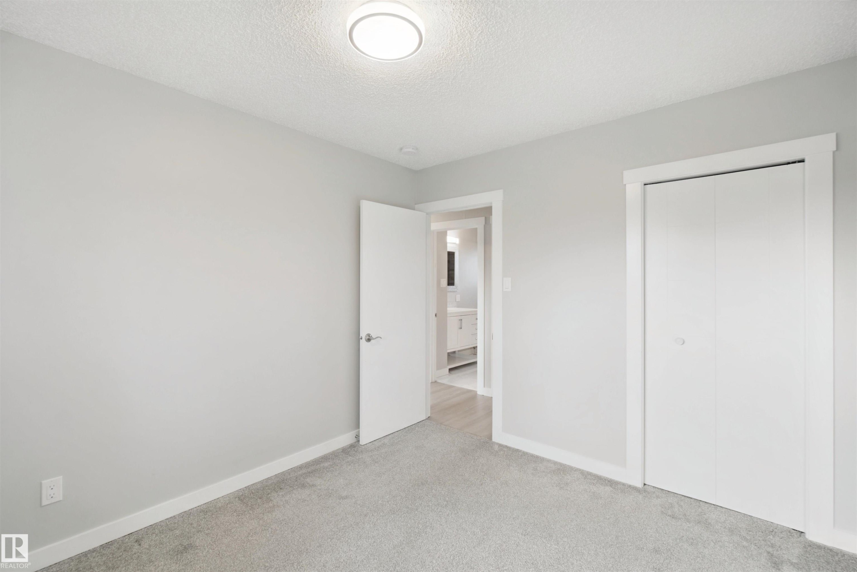 Soft grey carpeting, neutral wall color, contemporary flush-mount ceiling light, white bi-fold closet doors, and white interior door with polished chrome hardware - 13212 73 Street Nw, Edmonton, AB