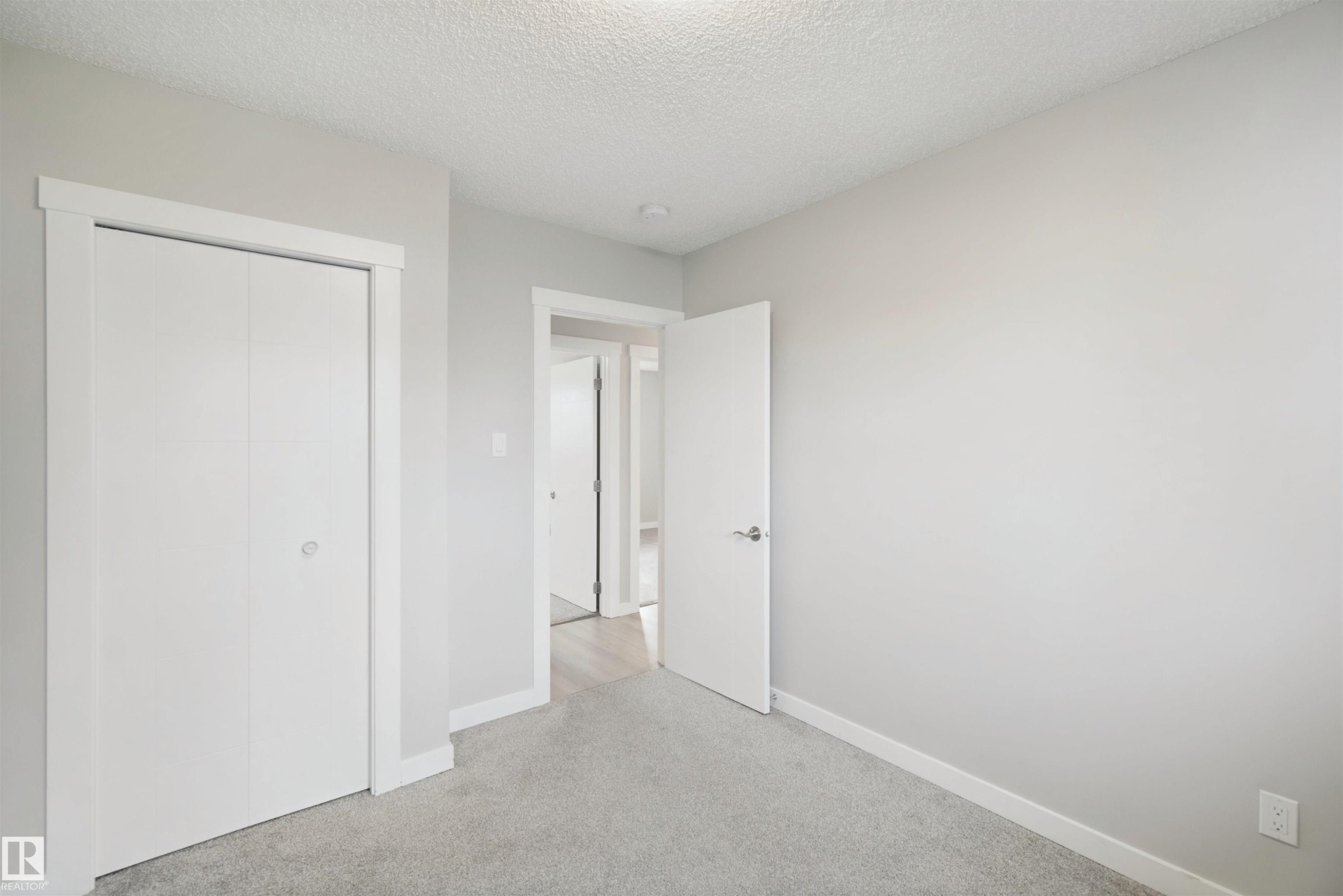 Wall-to-wall carpeting in a neutral tone, white bi-fold closet doors with white trim, and a white interior door - 13212 73 Street Nw, Edmonton, AB