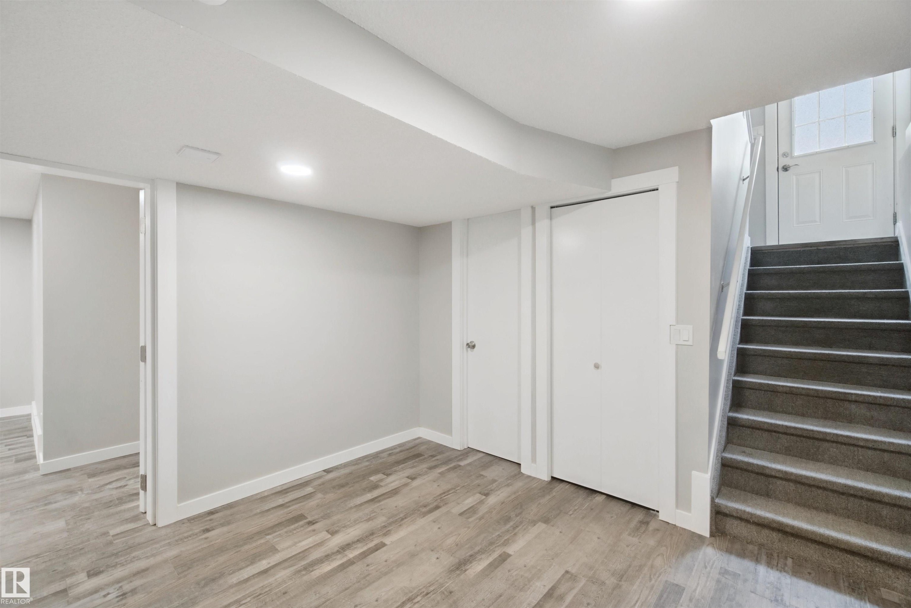 Wood-finish flooring, recessed ceiling lighting, two bi-fold closet doors, white interior doors, and a carpeted staircase - 13212 73 Street Nw, Edmonton, AB