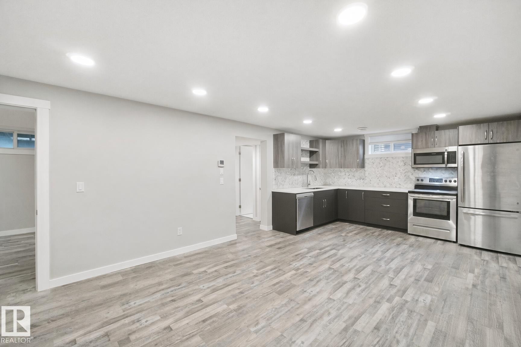 Contemporary kitchen featuring stainless steel appliances, grey cabinetry, light countertops, a patterned backsplash, and recessed lighting - 13212 73 Street Nw, Edmonton, AB