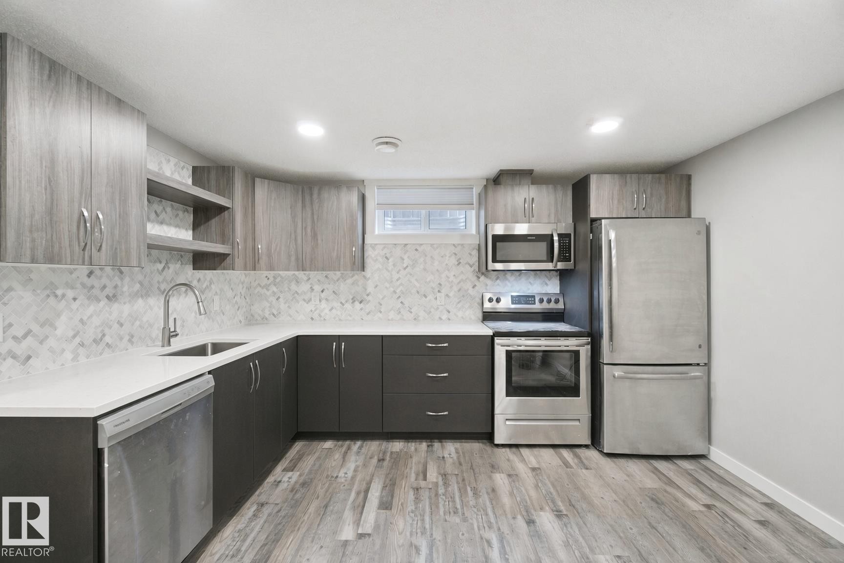 Modern kitchen featuring stainless steel appliances, wood-finish flooring, two-tone cabinetry, herringbone tile backsplash, and recessed lighting - 13212 73 Street Nw, Edmonton, AB