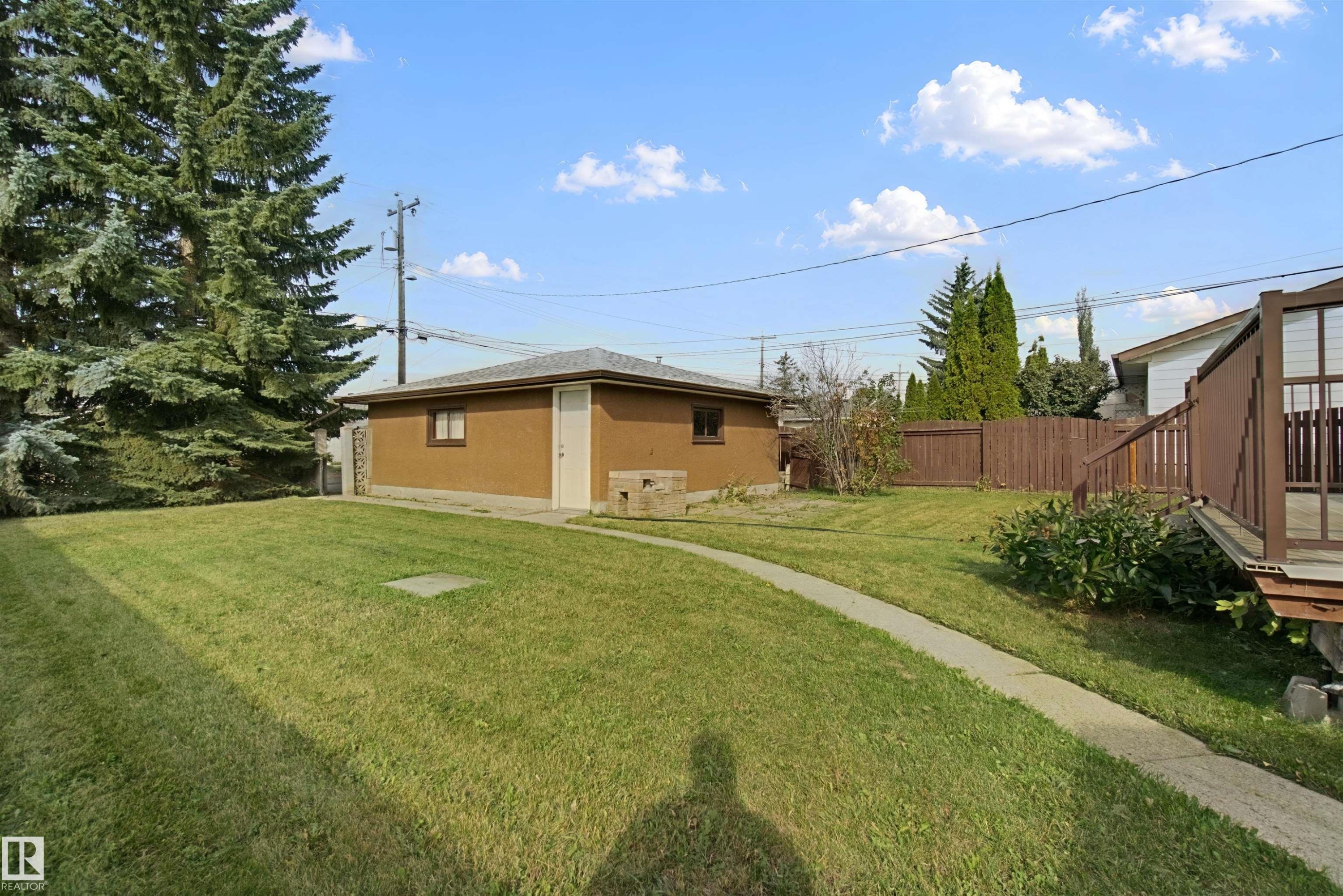 Expansive grassy yard featuring a concrete pathway, detached auxiliary building, wood privacy fencing, and mature trees - 13212 73 Street Nw, Edmonton, AB