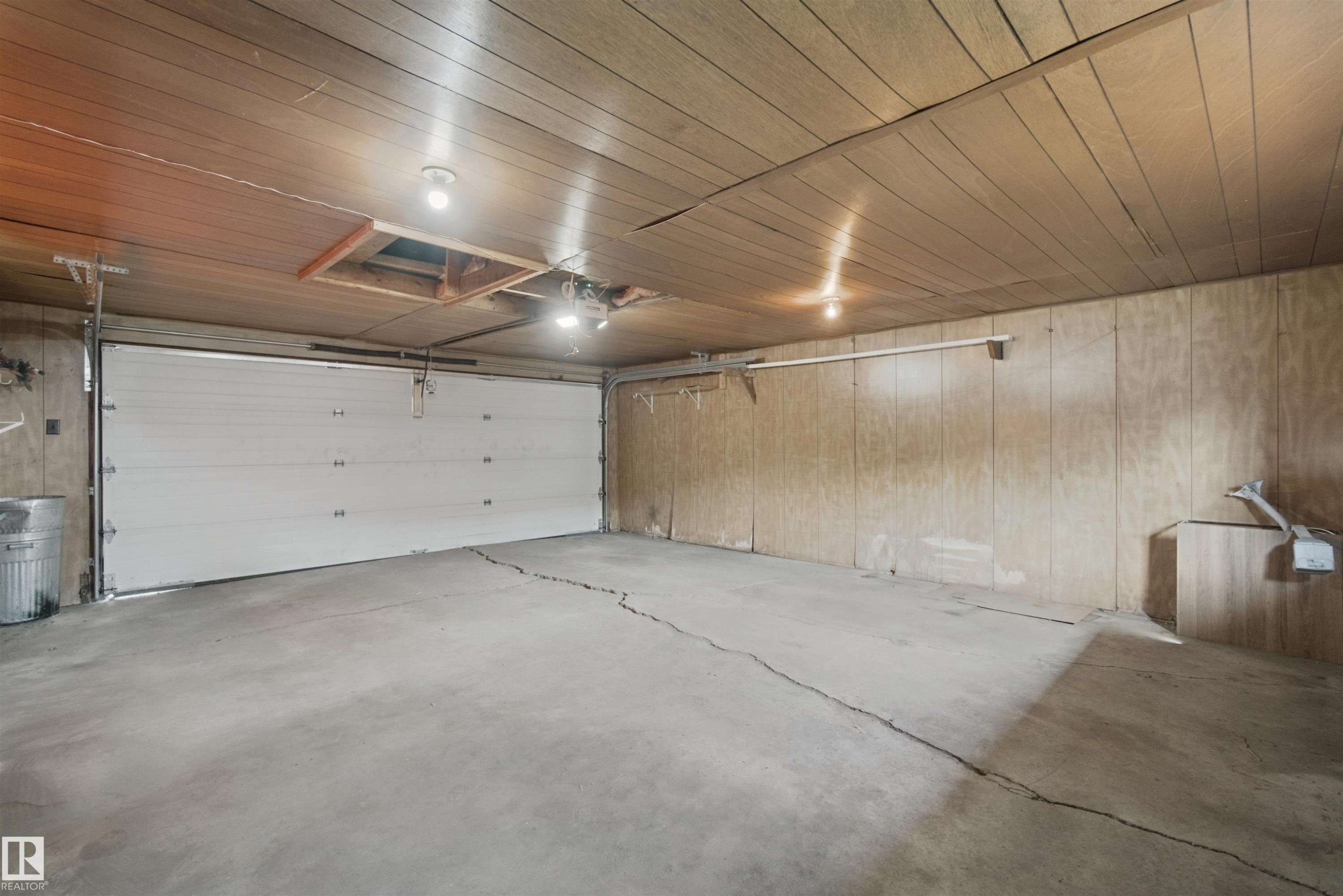 Attached garage featuring a concrete floor, wood-finish paneling, and overhead lighting - 13212 73 Street Nw, Edmonton, AB