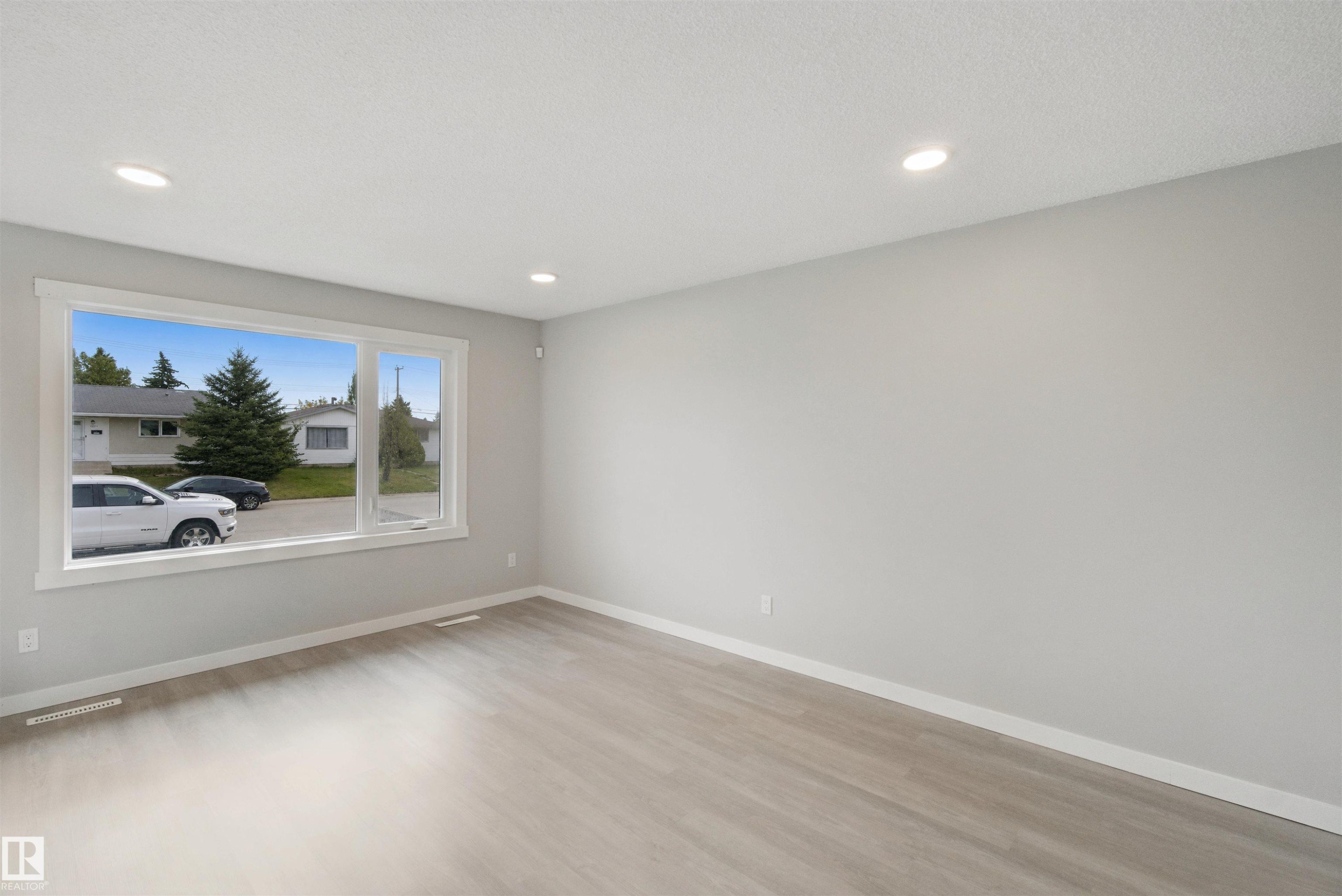 Spacious room featuring a large window, recessed lighting, light-toned walls, and wood-finish flooring - 13212 73 Street Nw, Edmonton, AB