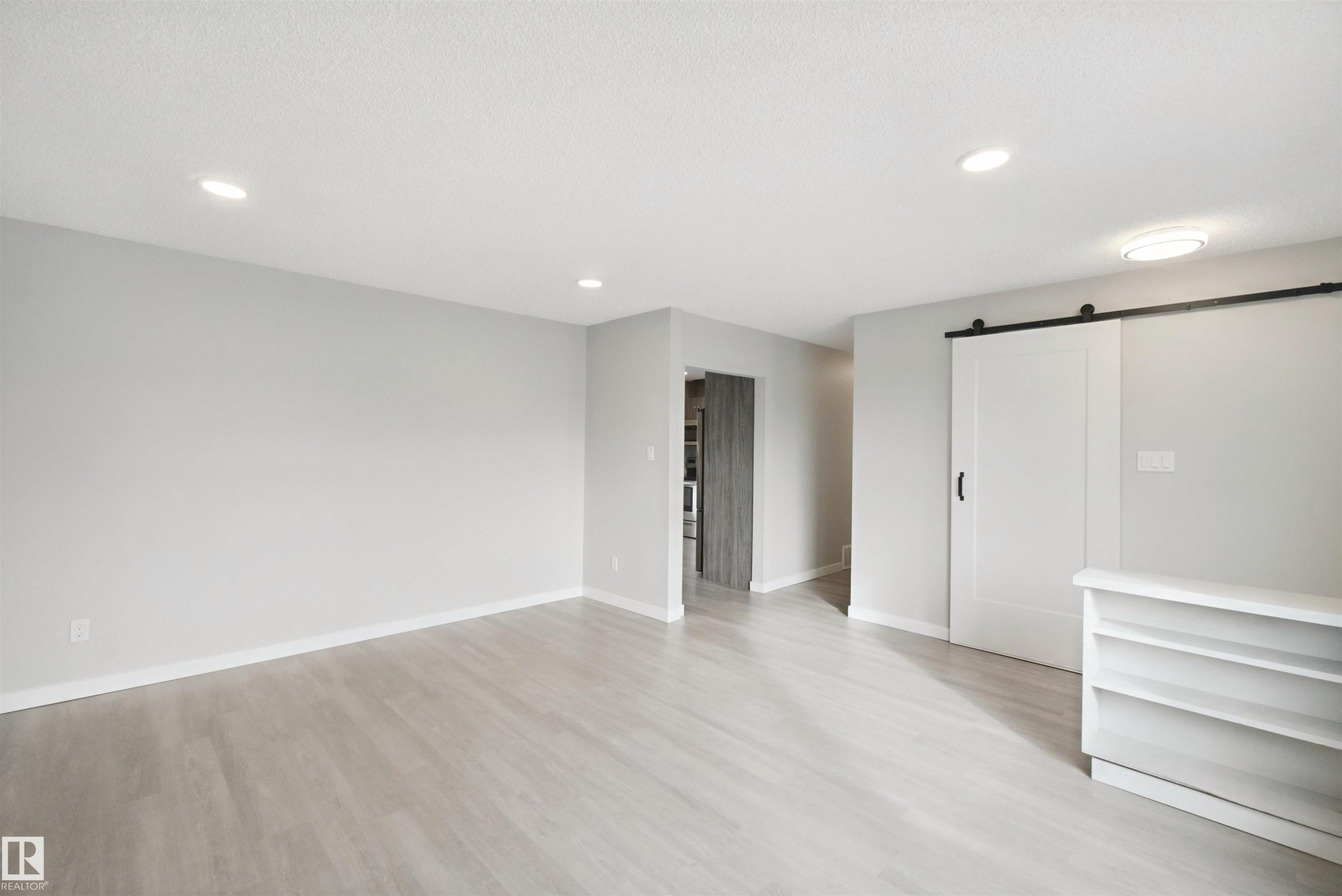 Wood-finish flooring, recessed lighting, and a white barn door with black hardware - 13212 73 Street Nw, Edmonton, AB