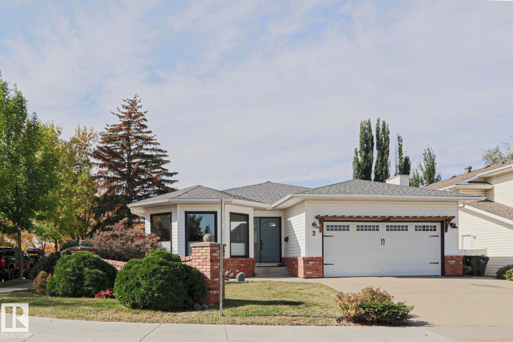 White siding exterior with brick accents, attached garage with decorative pergola, and mature landscaping - 2 Hillview Crescent, Sherwood Park, AB