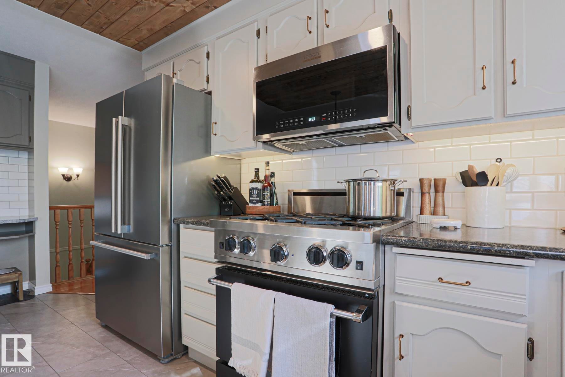Stainless steel appliances, subway tile backsplash, light-toned cabinetry, dark countertops, and wood-paneled ceiling - 2 Hillview Crescent, Sherwood Park, AB
