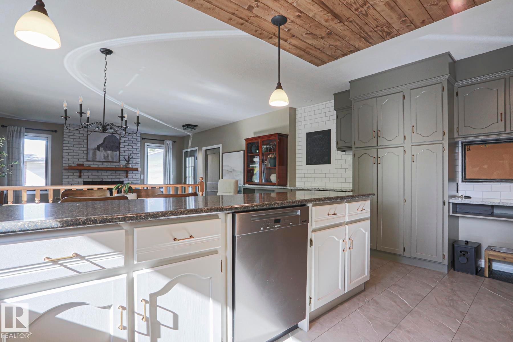 Kitchen island with stone countertop, integrated dishwasher, and white cabinetry - 2 Hillview Crescent, Sherwood Park, AB