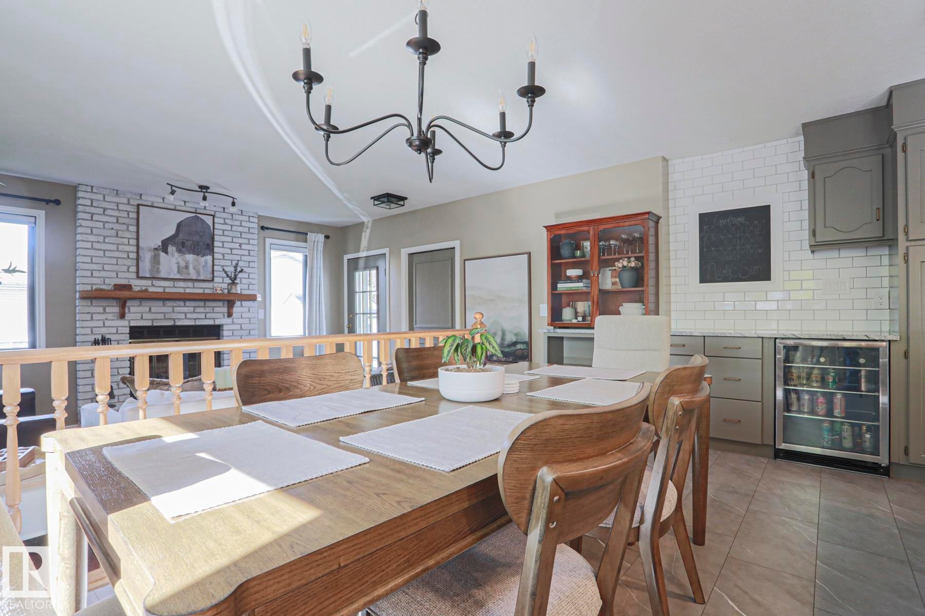 Exposed brick fireplace with a wood mantel, light wood-tone flooring, light grey cabinetry, subway tile backsplash, and a built-in beverage refrigerator - 2 Hillview Crescent, Sherwood Park, AB