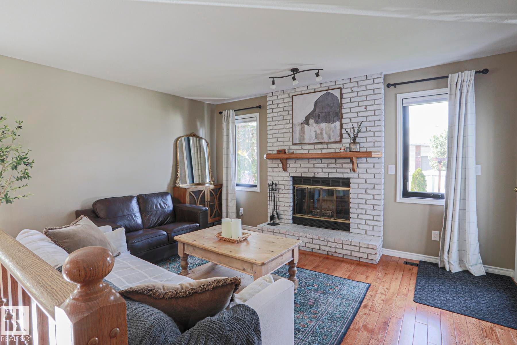 Living space featuring a whitewashed brick fireplace with a wood mantel, rich wood-finish flooring, and multiple windows - 2 Hillview Crescent, Sherwood Park, AB