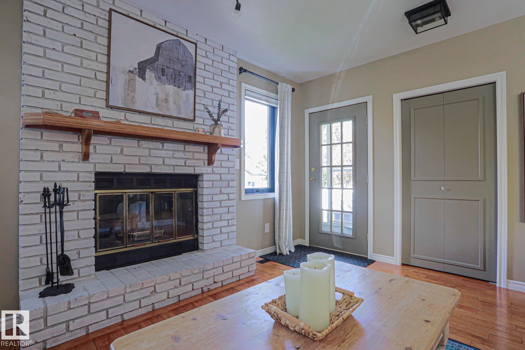 White-painted brick fireplace with a wood mantle and hearth, glass-paned door, and wood-finish flooring - 2 Hillview Crescent, Sherwood Park, AB