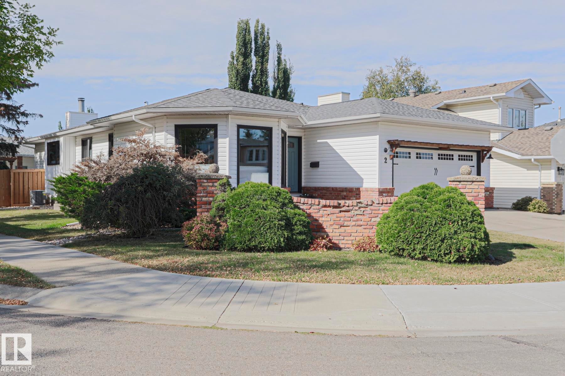 White siding exterior with a shingled roof, brick detailing, attached garage, and mature front landscaping - 2 Hillview Crescent, Sherwood Park, AB