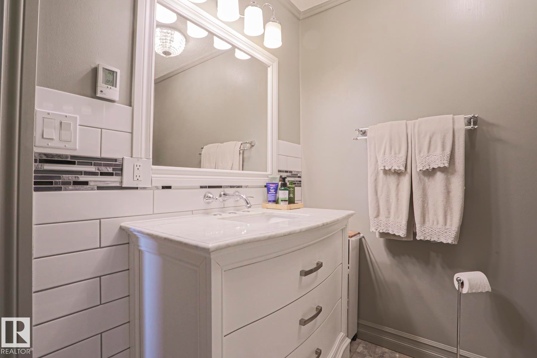 White vanity with an integrated sink, polished chrome faucet, and subway tile backsplash with an accent strip - 2 Hillview Crescent, Sherwood Park, AB