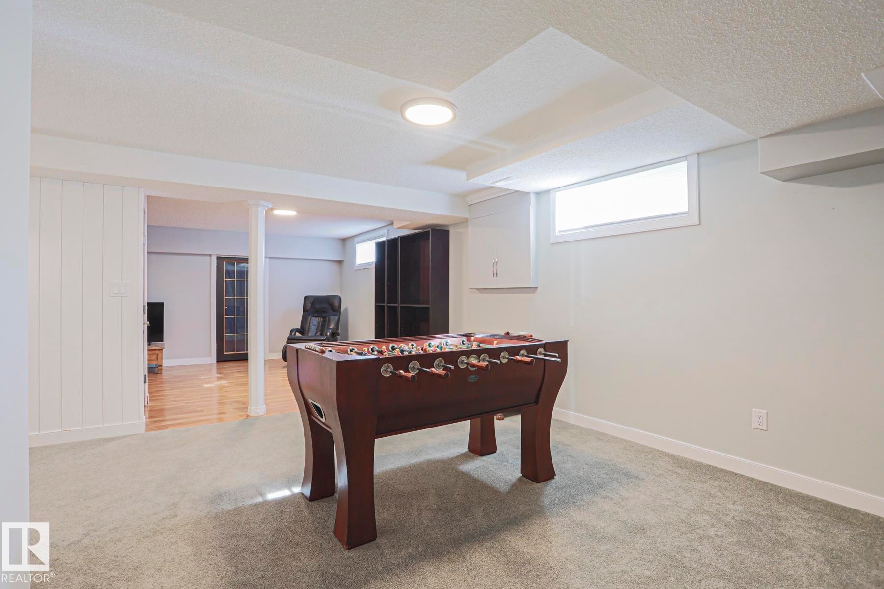 Carpeted recreation room featuring natural light, white trim, and a built-in storage cabinet - 2 Hillview Crescent, Sherwood Park, AB