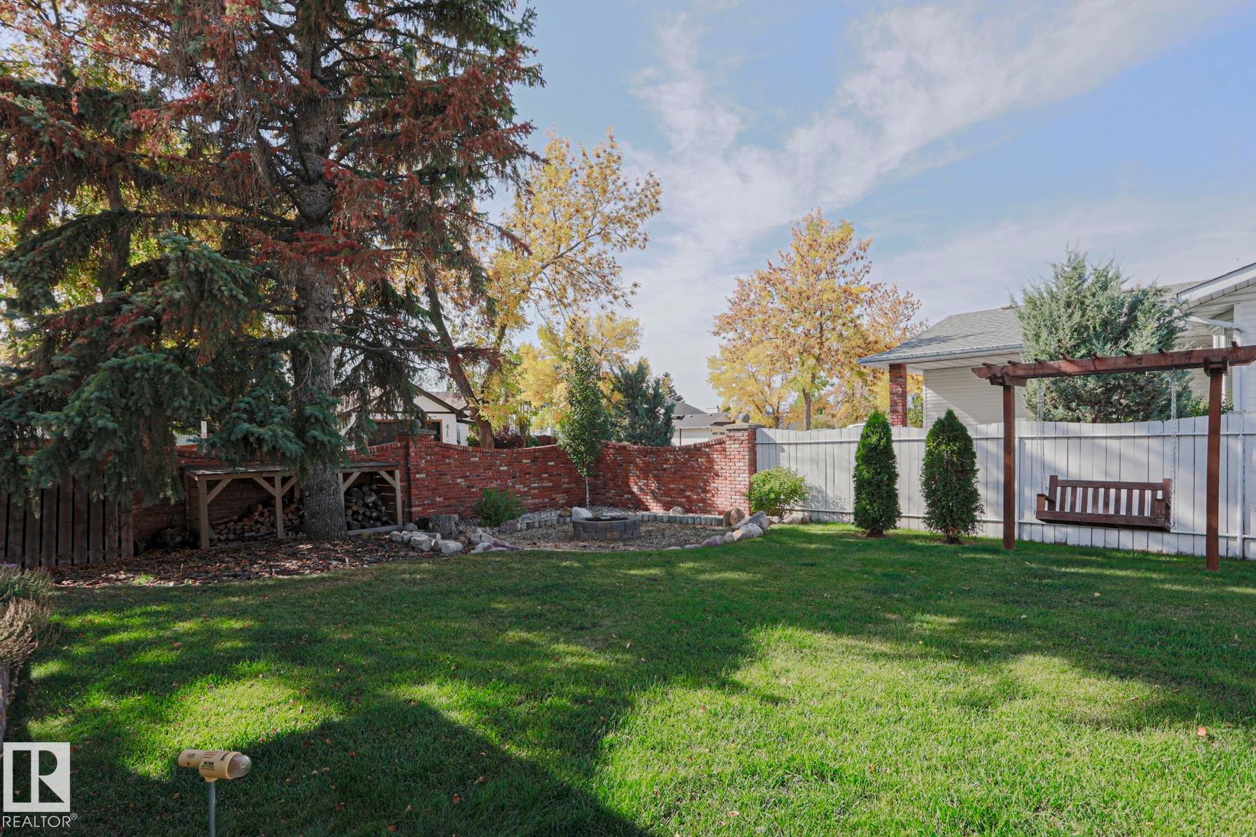 Expansive lawn area, framed by mature trees, a brick retaining wall, and a white panel fence - 2 Hillview Crescent, Sherwood Park, AB