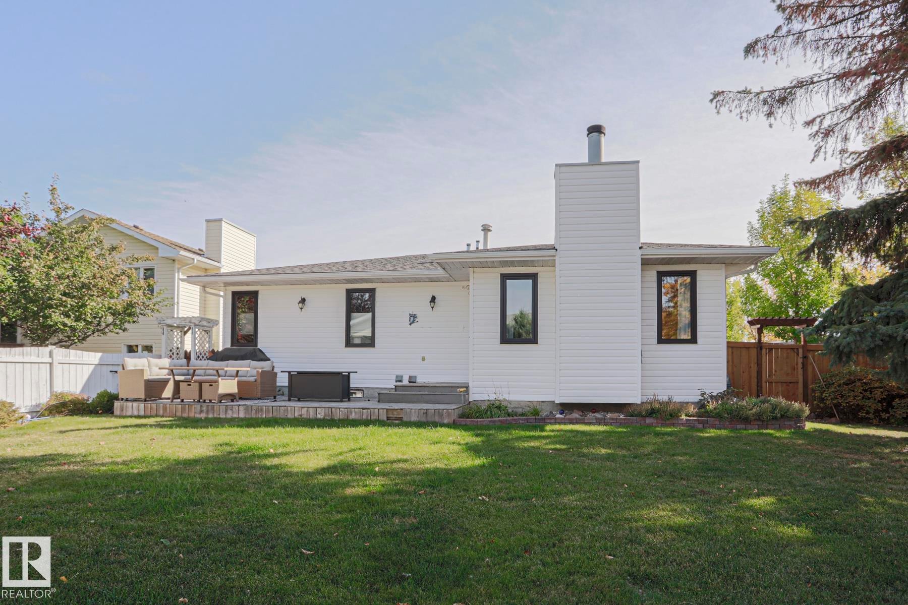 Expansive backyard featuring a manicured lawn, a large wood-finish patio, and a white privacy fence - 2 Hillview Crescent, Sherwood Park, AB