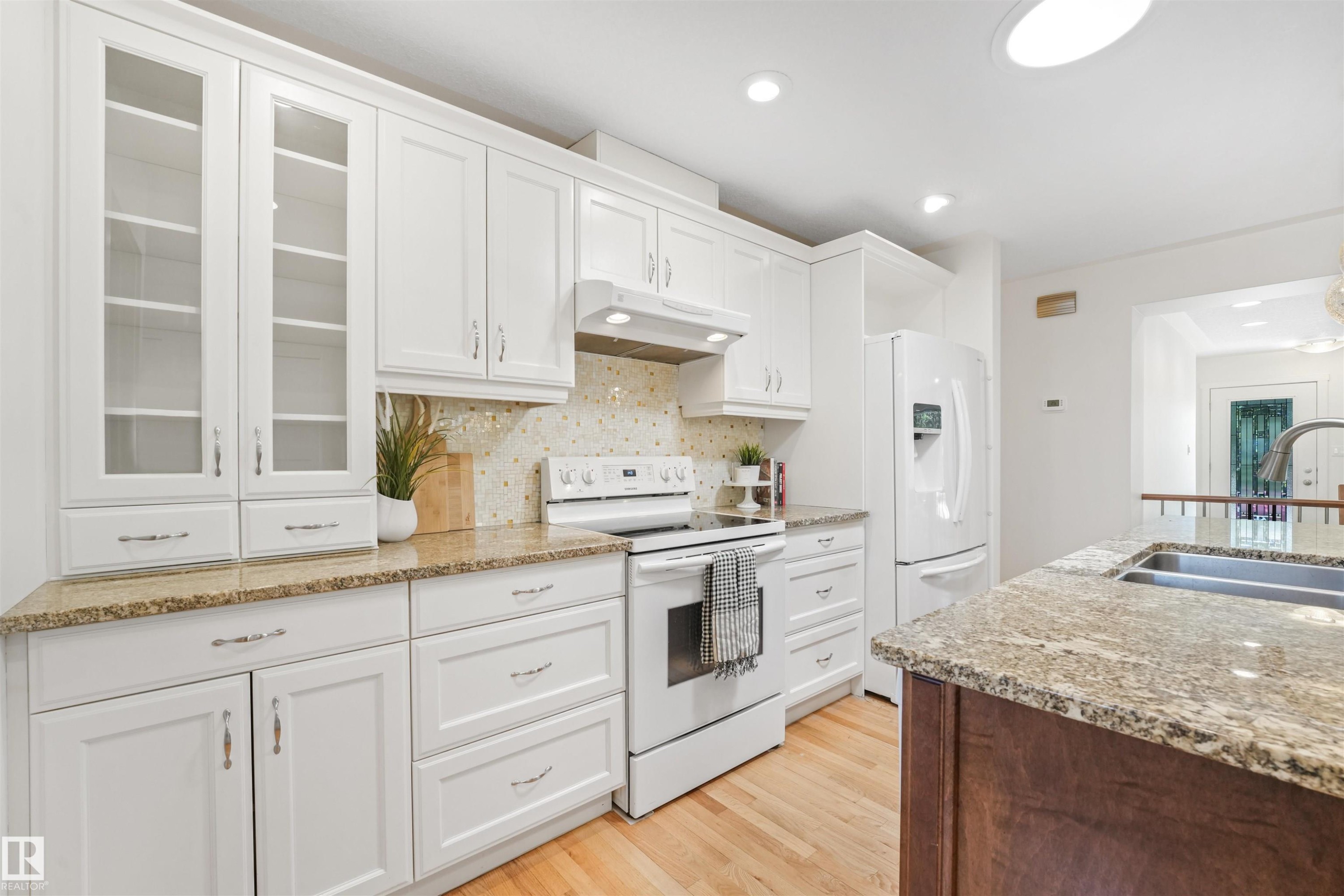 White cabinetry with glass-front uppers, light-toned countertops, and a tile backsplash - 8212 148 Street Nw, Edmonton, AB