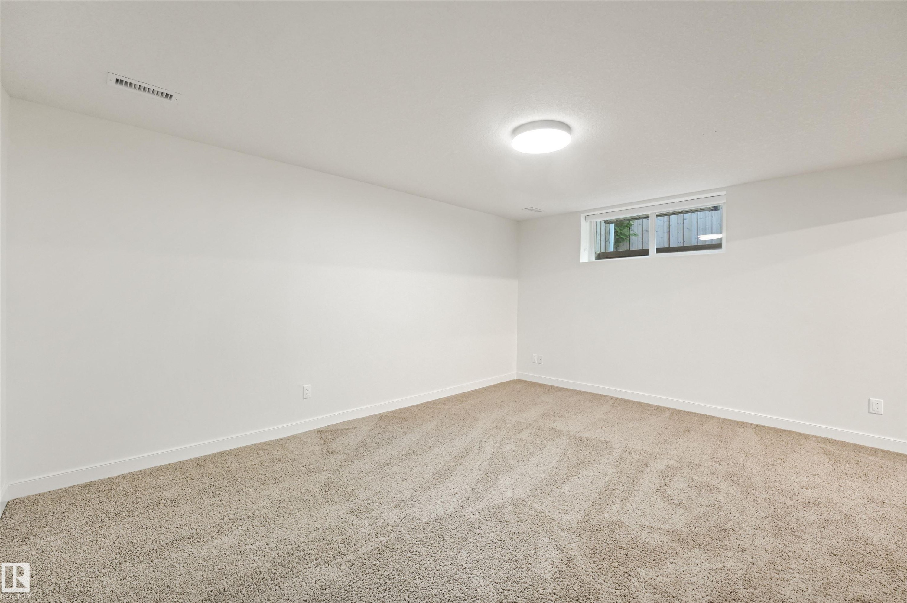 Neutral-toned carpeting, white painted walls, and a single window with privacy fencing - 8212 148 Street Nw, Edmonton, AB